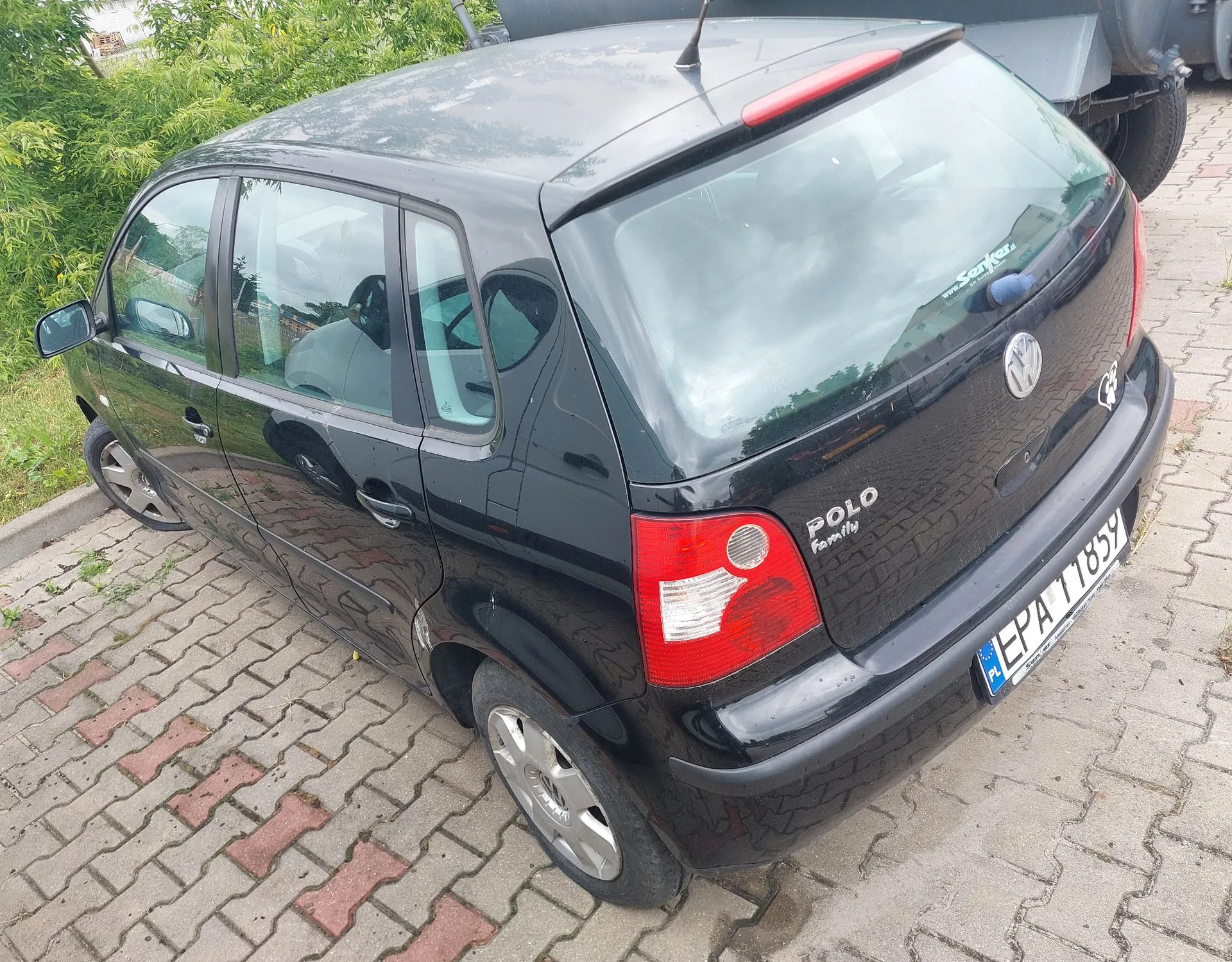Czarny samochód marki Volkswagen Polo zaparkowany na kostce brukowej. Widok z tyłu i z boku pojazdu. Na klapie bagażnika znajduje się logo Volkswagena oraz napisy 'POLO' i 'Family'. Samochód posiada polską tablicę rejestracyjną o numerze EPA 11859.