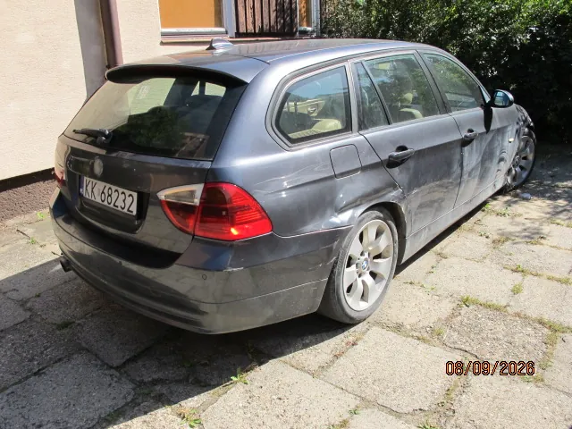 Szary samochód osobowy typu kombi zaparkowany na betonowym podjeździe. Pojazd posiada widoczne uszkodzenia karoserii w postaci wgnieceń na prawym tylnym błotniku oraz prawych drzwiach. Na tylnym zderzaku znajduje się tablica rejestracyjna o numerze KK 68232. W prawym dolnym rogu zdjęcia widnieje data 08/09/2026.