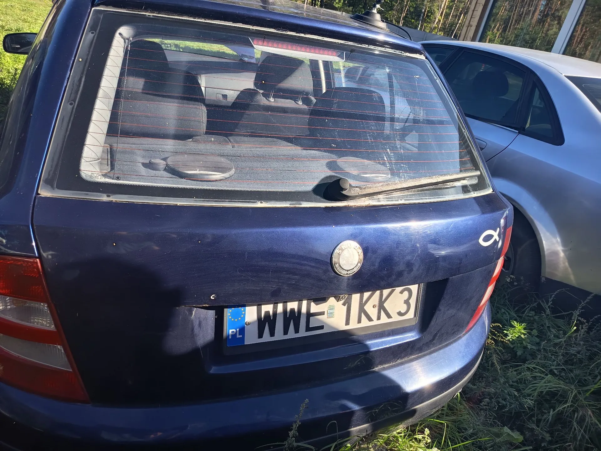 Tylny widok granatowego samochodu osobowego. Widoczna jest tylna szyba z ogrzewaniem, klapa bagażnika z logo marki oraz tablica rejestracyjna o numerze WWE 1KK3 z oznaczeniem PL. Obok stoi srebrny samochód.