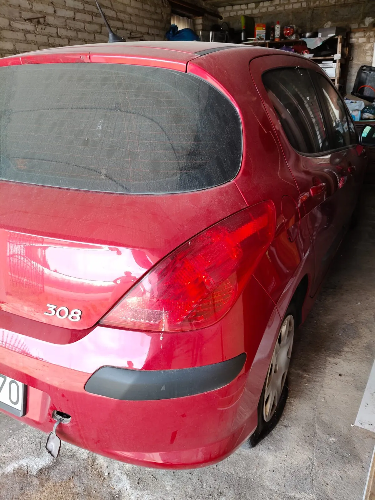 Tylny prawy bok czerwonego samochodu marki Peugeot, model 308. Widoczna jest tylna szyba, prawe światło tylne oraz fragment zderzaka z czarnym plastikowym elementem. Na klapie bagażnika znajduje się srebrny napis '308'. Samochód zaparkowany jest w garażu.
