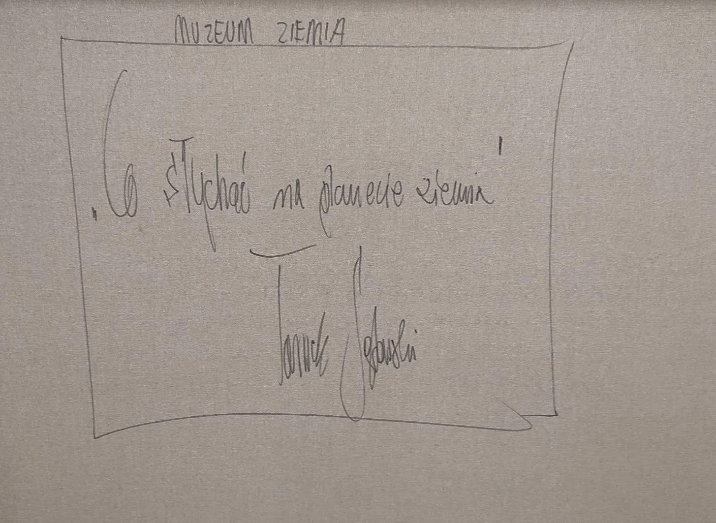 Ręcznie napisany tekst na szarym tle, ujęty w prostokątną ramkę. Na górze, poza ramką, widnieje napis „MUZEUM ZIEMIA”. Wewnątrz ramki znajduje się zdanie „Co słuchać na planecie ziemia” oraz podpis poniżej: „Tomek Sebastian”.