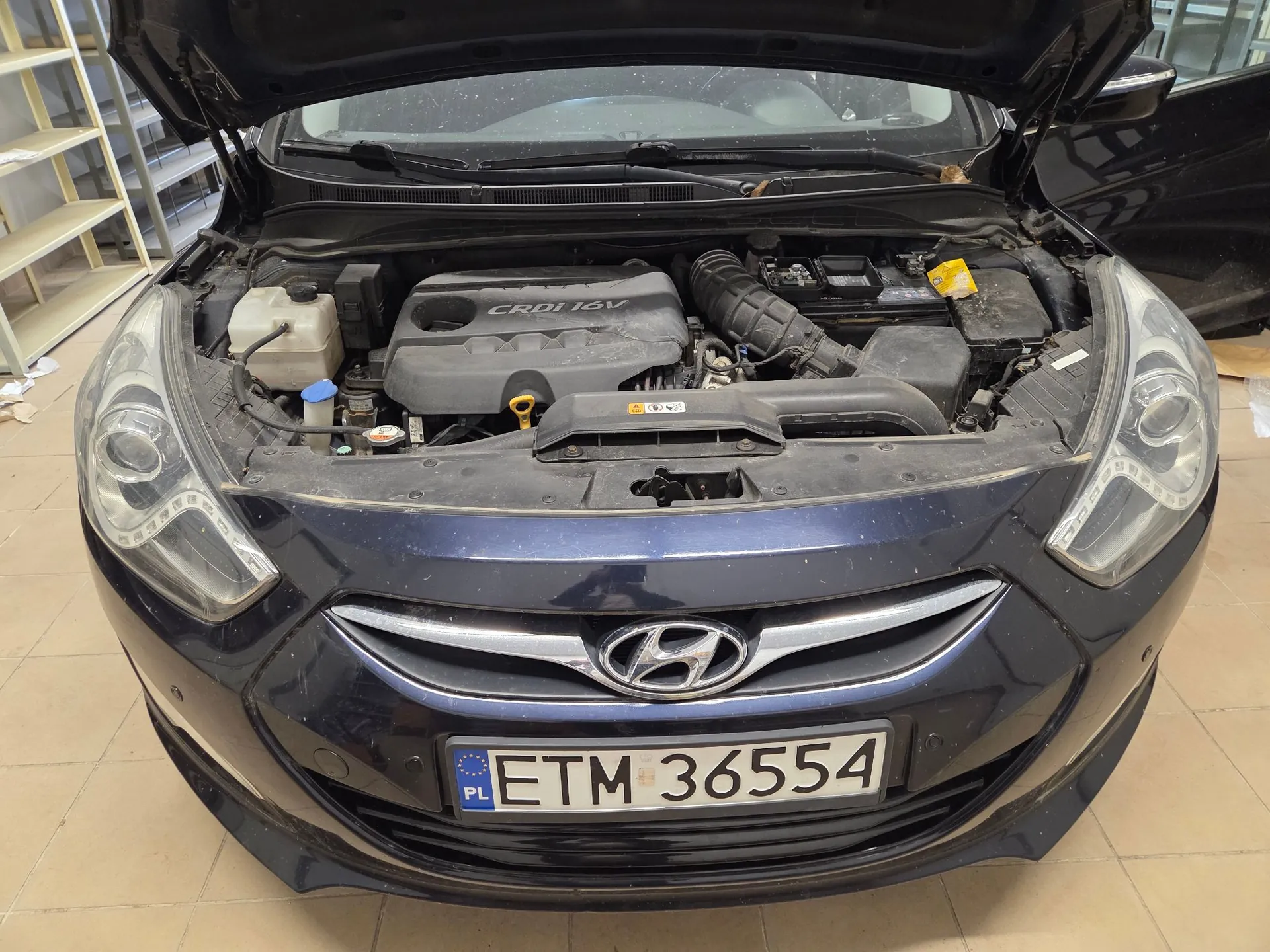 Widok z przodu ciemnoniebieskiego samochodu marki Hyundai z otwartą maską, ukazującą silnik z napisem CRDi 16V. Na przednim zderzaku znajduje się polska tablica rejestracyjna o numerze ETM 36554.