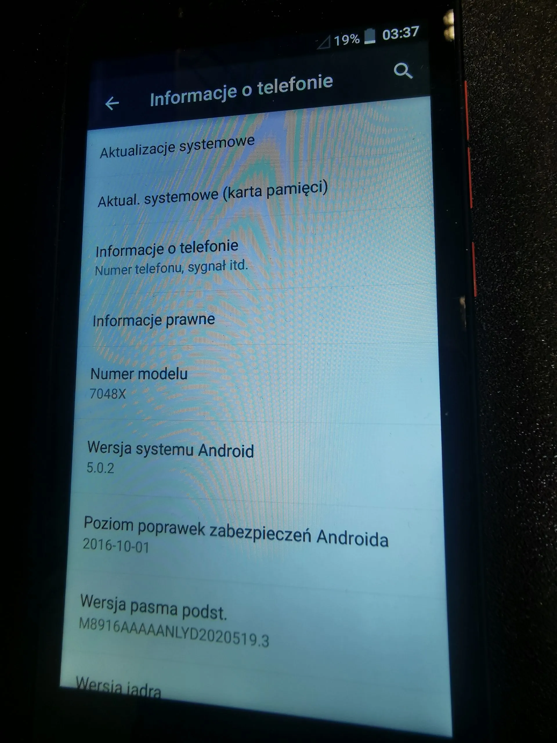 Zdjęcie ekranu smartfona wyświetlającego menu 'Informacje o telefonie'. Na ekranie widoczne są następujące opcje i dane: 'Aktualizacje systemowe', 'Aktual. systemowe (karta pamięci)', 'Informacje o telefonie (Numer telefonu, sygnał itd.)', 'Informacje prawne', 'Numer modelu: 7048X', 'Wersja systemu Android: 5.0.2', 'Poziom poprawek zabezpieczeń Androida: 2016-10-01', 'Wersja pasma podst.: M8916AAAAANLYD2020519.3' oraz fragment napisu 'Wersja jądra'. W górnym pasku widoczna jest godzina 03:37 i poziom baterii 19%.