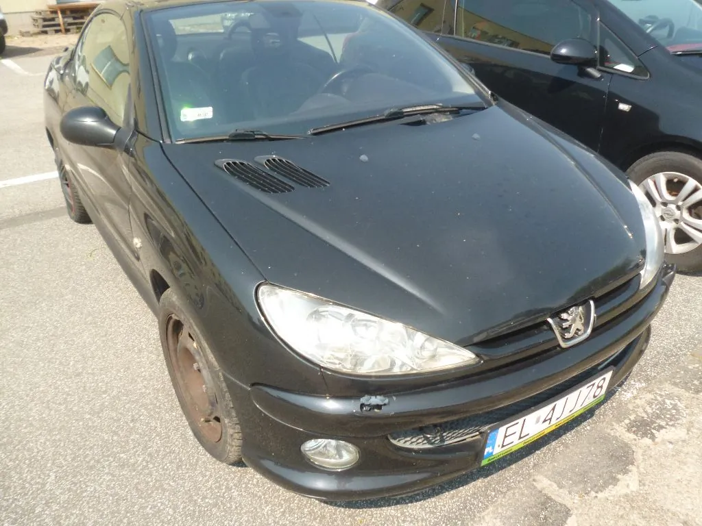 Czarny samochód osobowy marki Peugeot zaparkowany na asfaltowym placu. Widoczny jest przód pojazdu z tablicą rejestracyjną o numerze EL 41178. Obok stoi inny, czarny samochód.