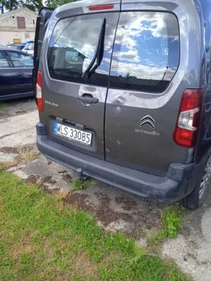 Tylna część szarego samochodu marki Citroën z otwartymi drzwiami tylnymi. Pojazd posiada polską tablicę rejestracyjną o numerze WLS 33085. Samochód zaparkowany jest na betonowym podłożu z kępami trawy.