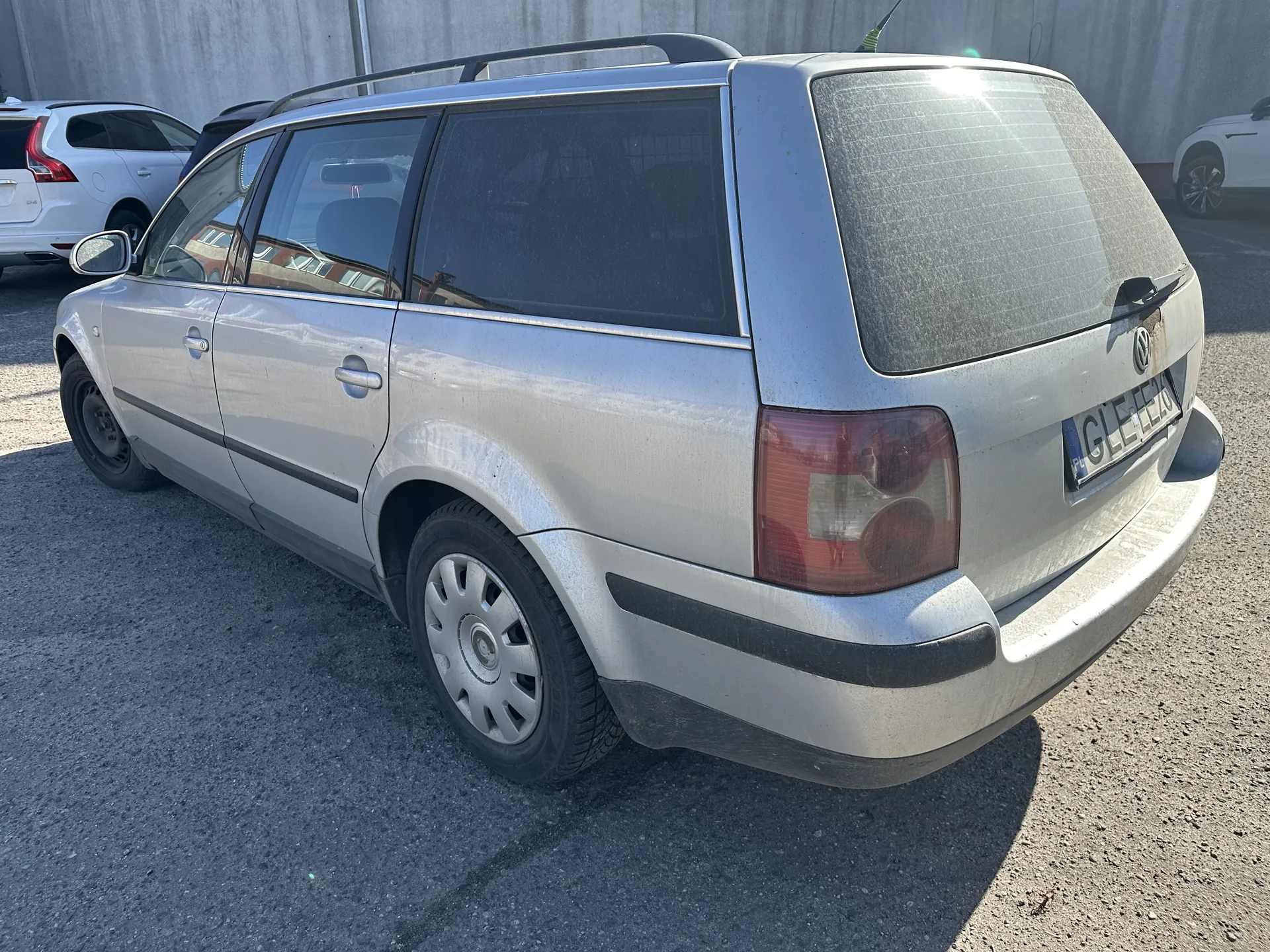 Srebrny samochód typu kombi marki Volkswagen zaparkowany na asfaltowym placu. Widoczna tablica rejestracyjna PL GLE 12A, dachówka, przyciemniane szyby oraz lekko zabrudzony tylny zderzak. W tle białe samochody i betonowa ściana.