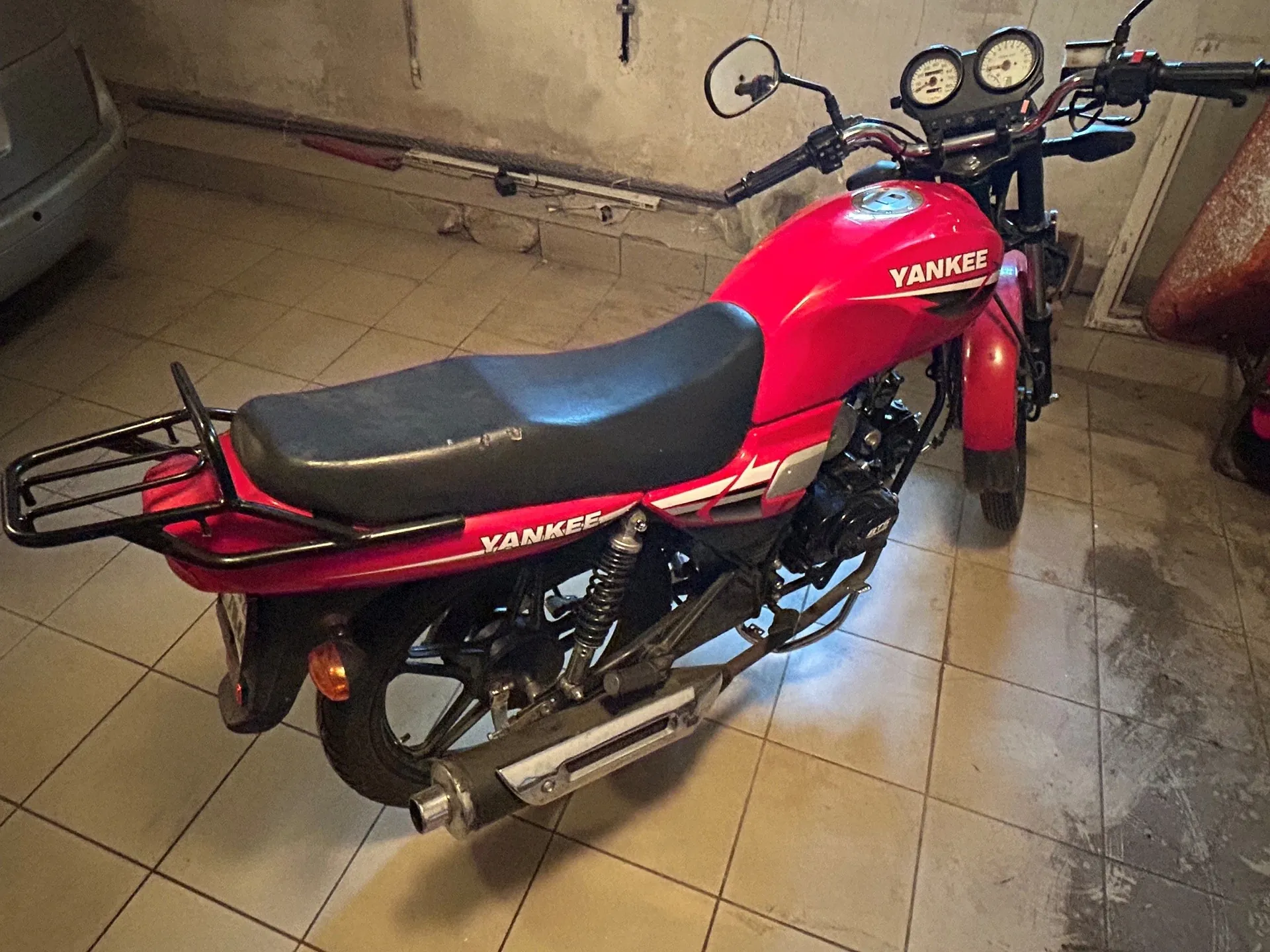 Czerwony motocykl marki Yankee zaparkowany w pomieszczeniu z kafelkami na podłodze. Pojazd posiada czarne siedzenie, tylny bagażnik oraz srebrną rurę wydechową. Na baku i bocznej owiewce widnieje biały napis 'YANKEE'.
