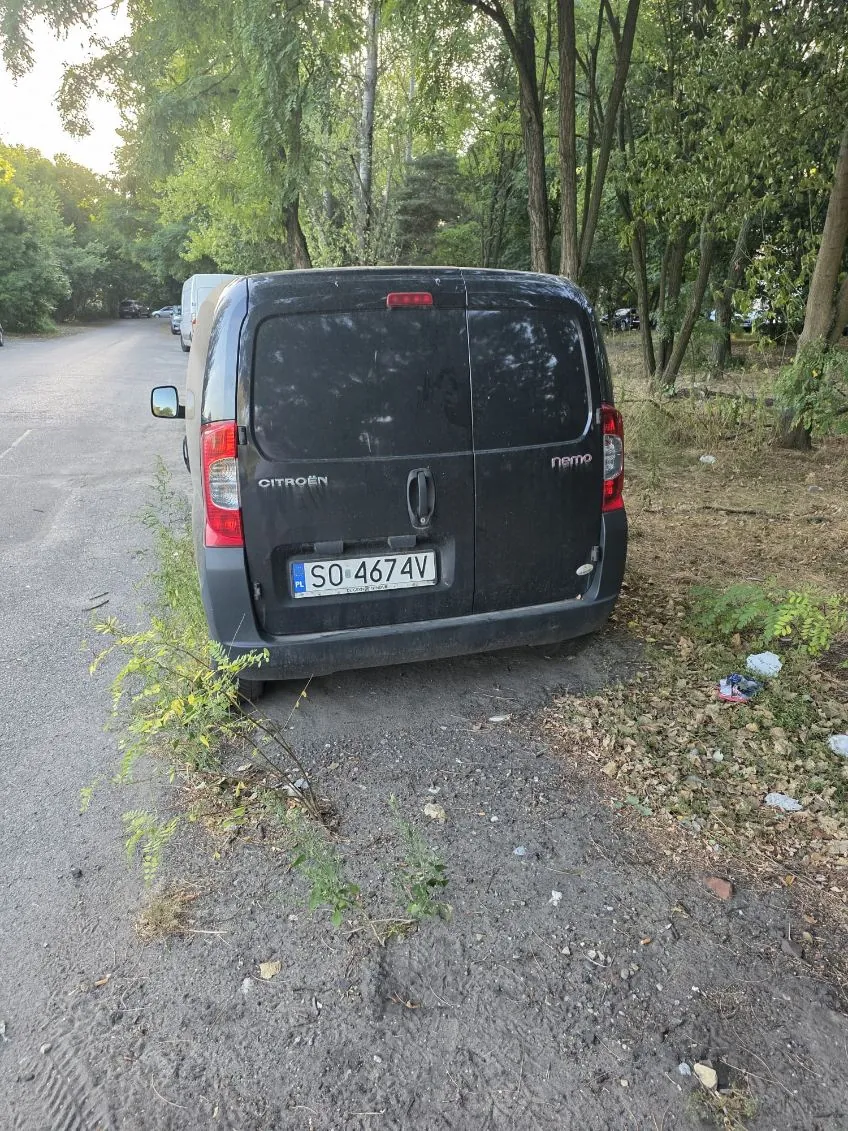 Czarny samochód dostawczy marki Citroën Nemo zaparkowany na poboczu drogi, obok zielonych drzew i krzewów. Widoczna jest tablica rejestracyjna o numerze SO 4674V.