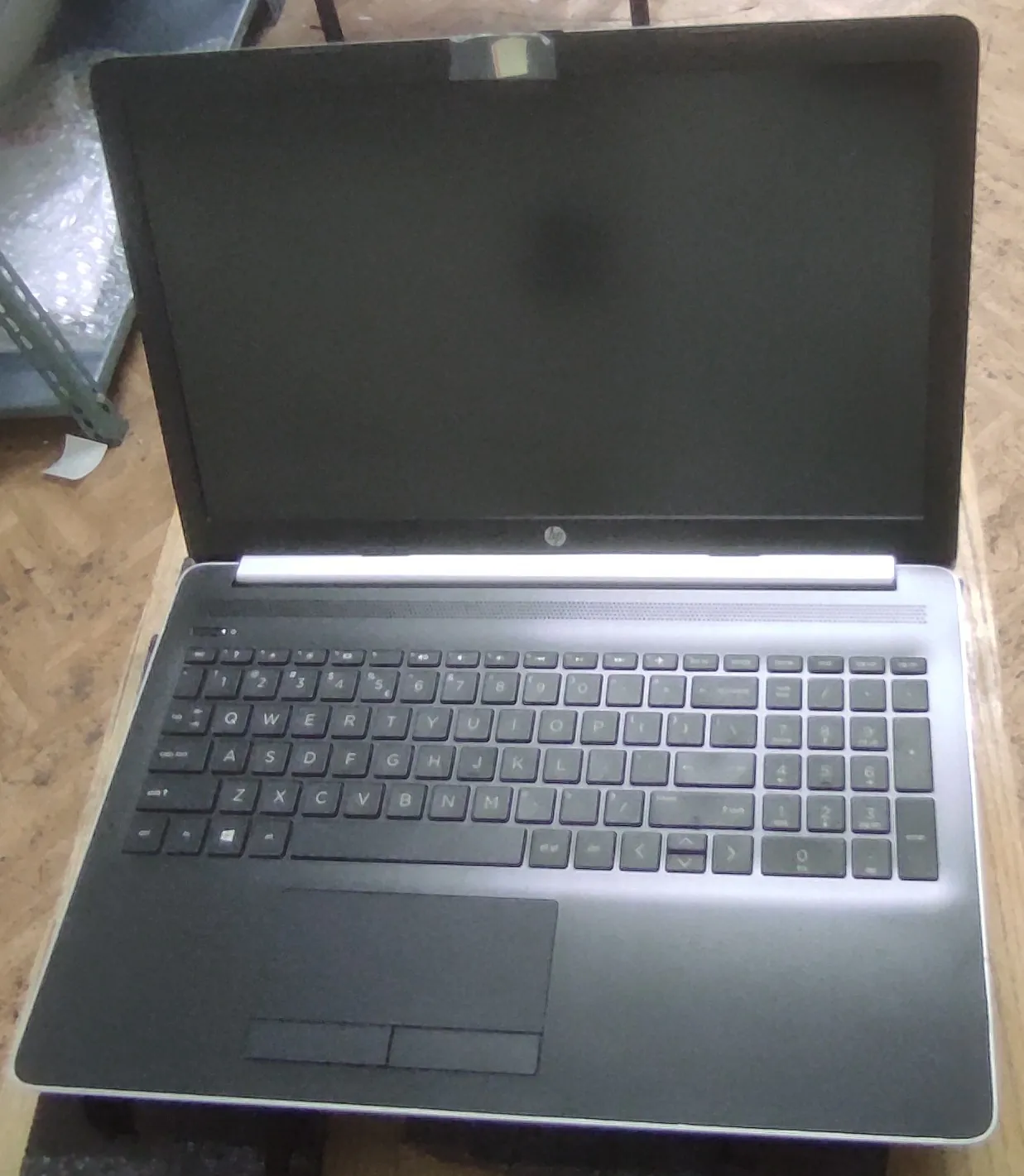 Otwarty laptop marki HP z czarnym ekranem i ciemnoszarą klawiaturą, ustawiony na drewnianej powierzchni.