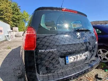 Tylny widok czarnego samochodu marki Peugeot. Na klapie bagażnika widnieje napis PEUGEOT oraz logo marki. Samochód posiada polską tablicę rejestracyjną o numerze FSW MT94. Po prawej stronie widoczny jest fragment innego, niebieskiego samochodu.