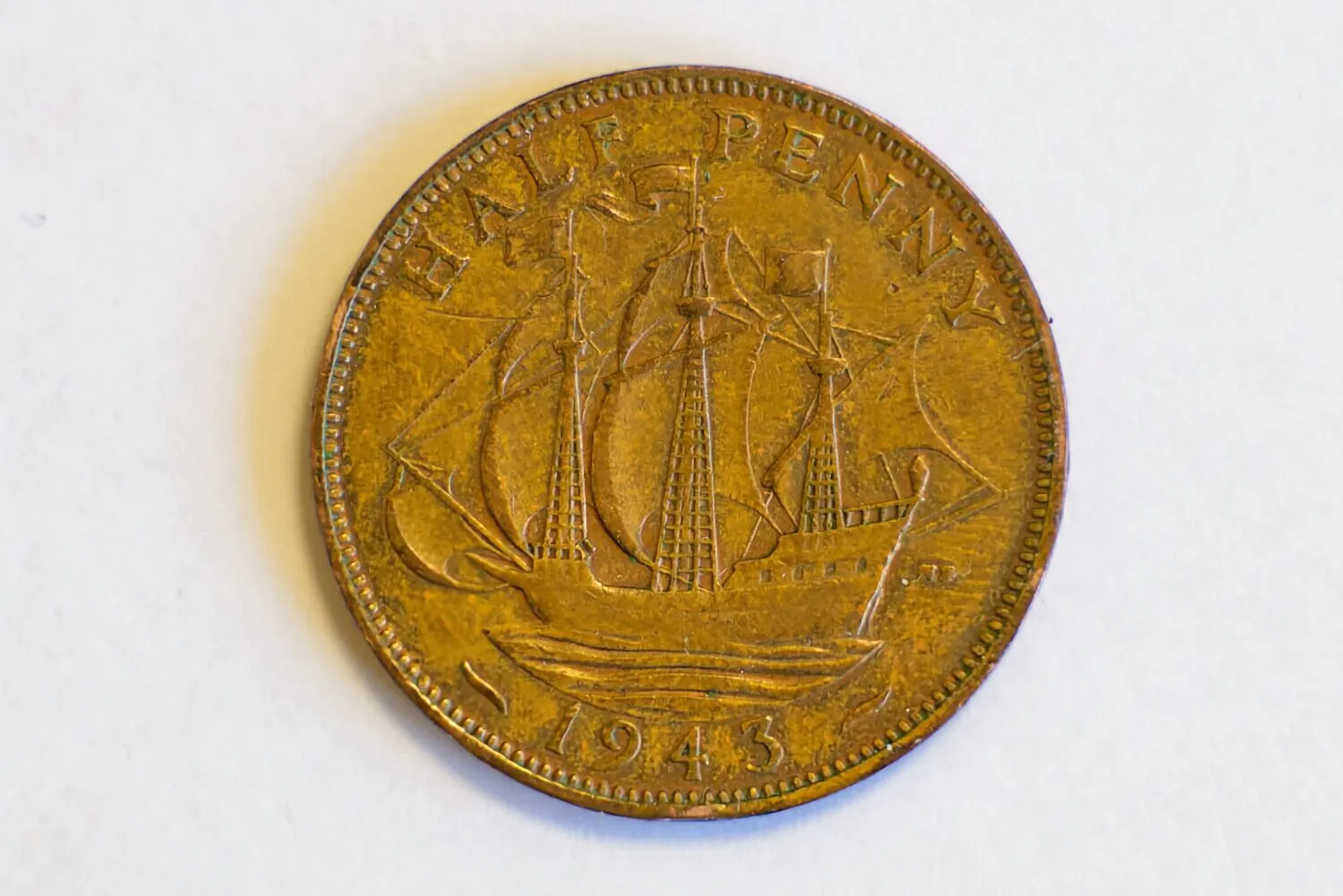Zdjęcie miedzianej monety o nominale HALF PENNY z 1943 roku. W centrum monety znajduje się wizerunek żaglowca z rozpostartymi żaglami. Na górnym brzegu widnieje napis „HALF PENNY”, a na dolnym rok emisji „1943”.