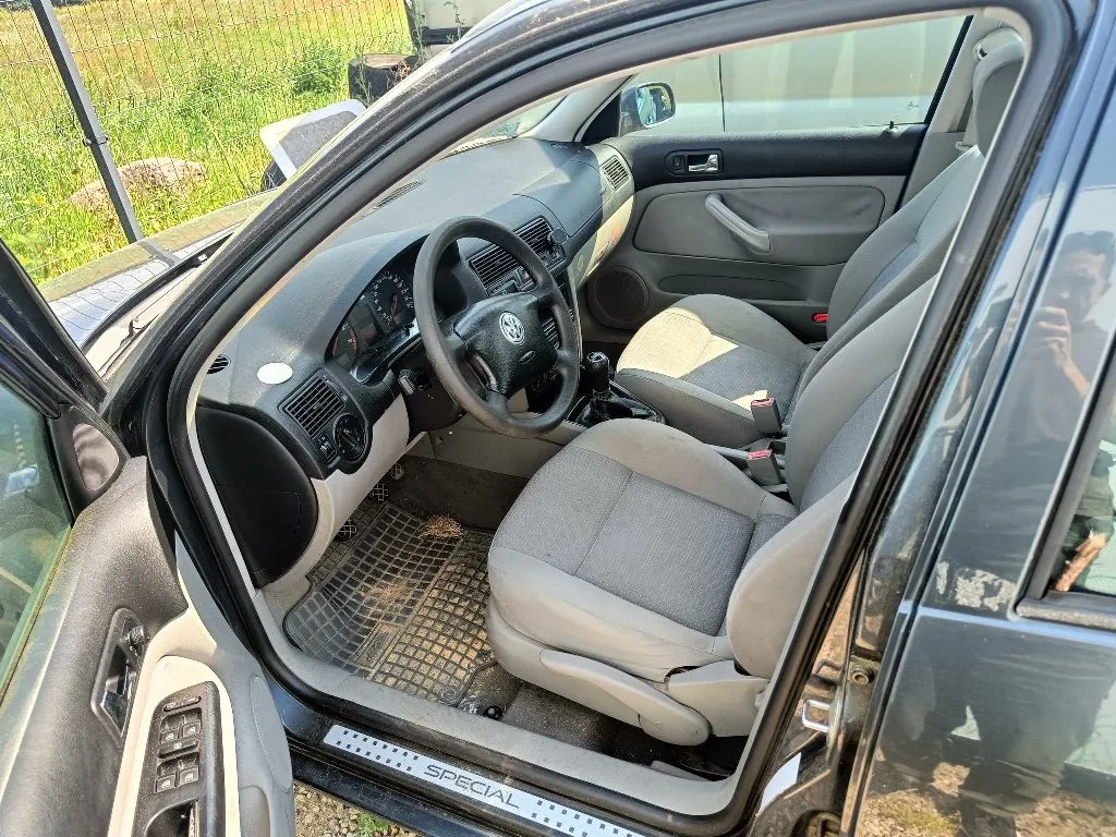 Wnętrze ciemnego samochodu widziane z otwartych drzwi kierowcy. Widoczna szara tapicerka foteli, kierownica z logo Volkswagena, deska rozdzielcza oraz gumowa mata na podłodze. Na progu samochodu znajduje się napis 'SPECIAL'.
