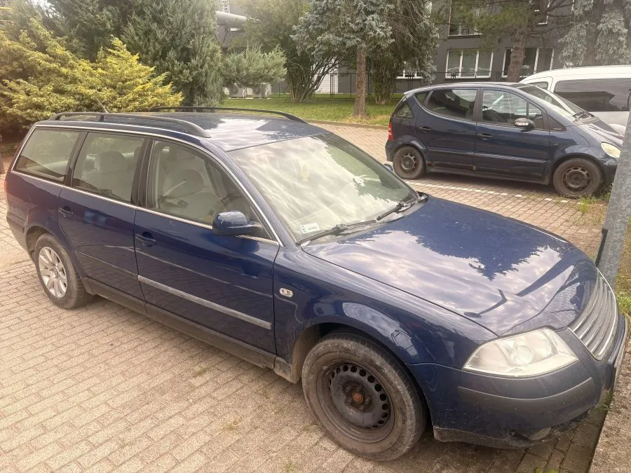 Niebieski samochód osobowy typu kombi zaparkowany na kostce brukowej. Obok niego stoi ciemnoniebieski samochód kompaktowy. W tle widoczne są zielone drzewa i fragmenty budynków mieszkalnych.