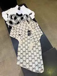 Biała koszula z czarnym powtarzającym się geometrycznym wzorem, obok czarno-biała szachownicowa tkanina. Obie leżą na ciemnej powierzchni, na tle jasnej podłogi.