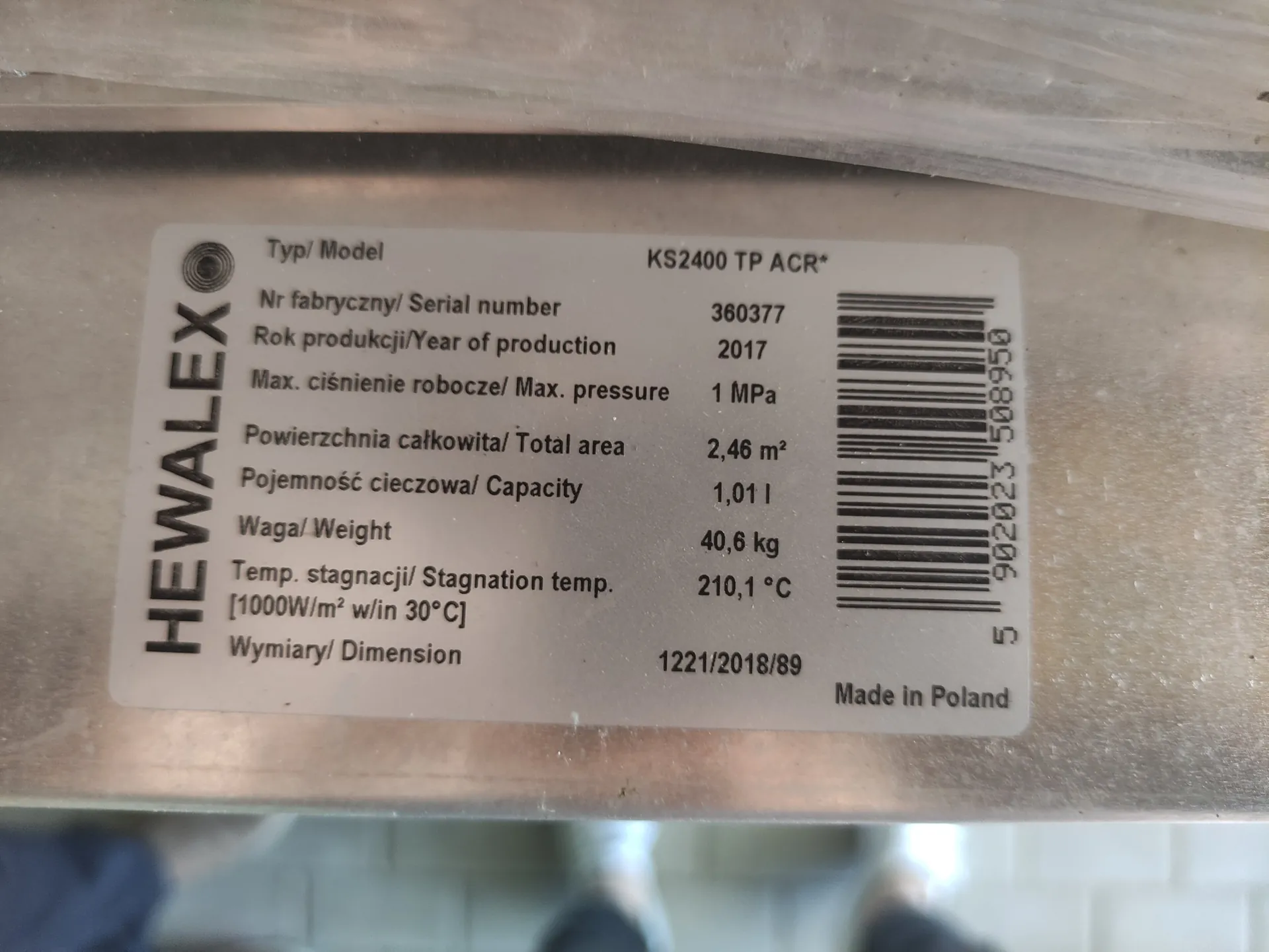 Zdjęcie tabliczki znamionowej urządzenia marki HEWALEX. Tabliczka zawiera następujące dane: Typ/ Model: KS2400 TP ACR*, Nr fabryczny/ Serial number: 360377, Rok produkcji/Year of production: 2017, Max. ciśnienie robocze/ Max. pressure: 1 MPa, Powierzchnia całkowita/ Total area: 2,46 m², Pojemność cieczowa/ Capacity: 1,01 l, Waga/ Weight: 40,6 kg, Temp. stagnacji/ Stagnation temp. [1000W/m² w/in 30°C]: 210,1 °C, Wymiary/ Dimension: 1221/2018/89. Po prawej stronie znajduje się kod kreskowy z numerem 5 902023 508950. Na dole widnieje napis 'Made in Poland'.