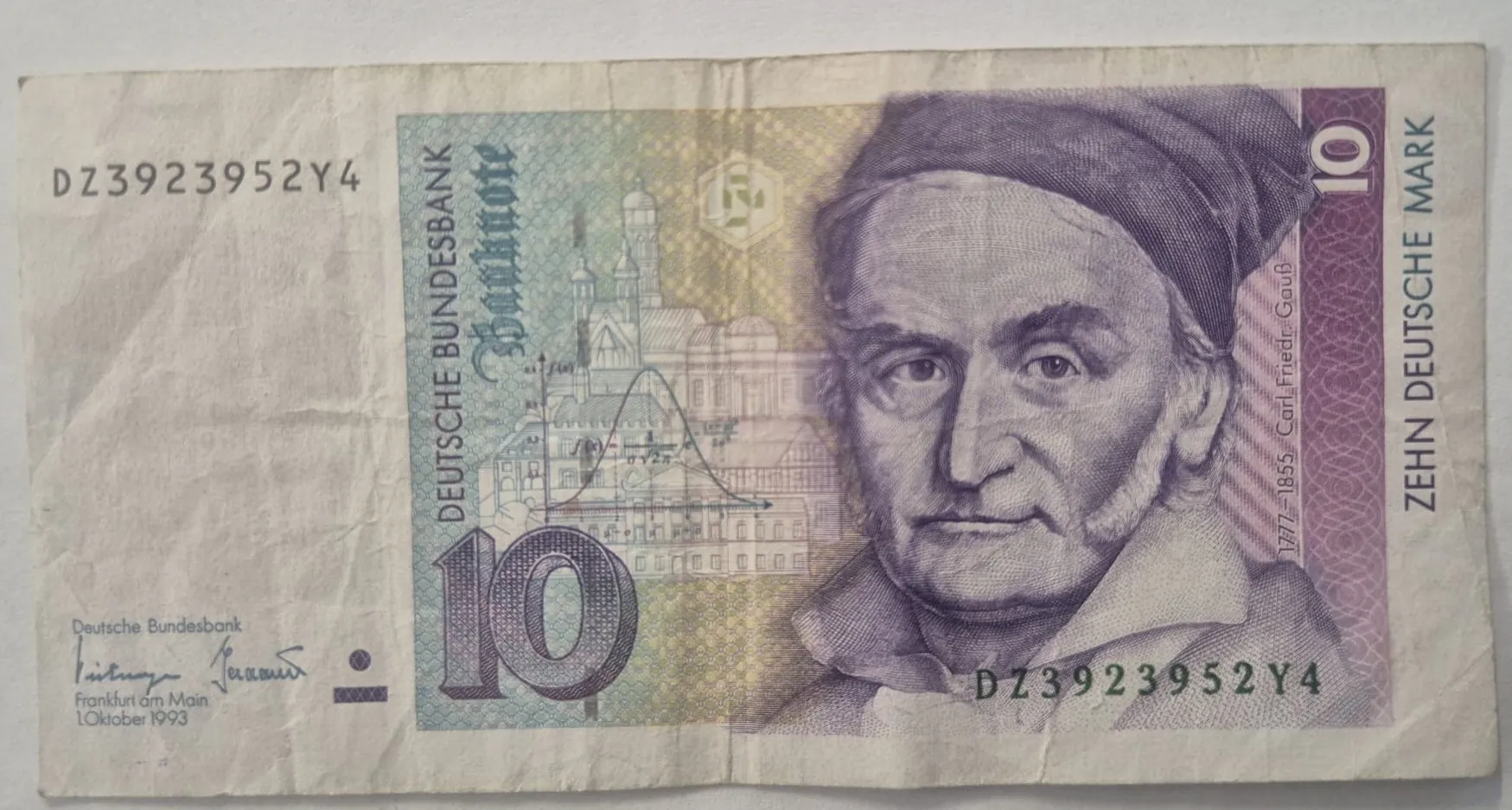 Niemiecki banknot o nominale 10 marek niemieckich (Zehn Deutsche Mark). Po prawej stronie znajduje się portret Carla Friedricha Gaussa w fioletowej kolorystyce. Po lewej stronie widnieje duża liczba 10 oraz rysunek budynków i wykres matematyczny. Na banknocie widnieją napisy: 'DEUTSCHE BUNDESBANK', 'Banknote', 'ZEHN DEUTSCHE MARK' oraz numer seryjny 'DZ3923952Y4' powtórzony w dwóch miejscach. W lewym dolnym rogu znajduje się data '1 Oktober 1993' oraz miejsce wydania 'Frankfurt am Main'.