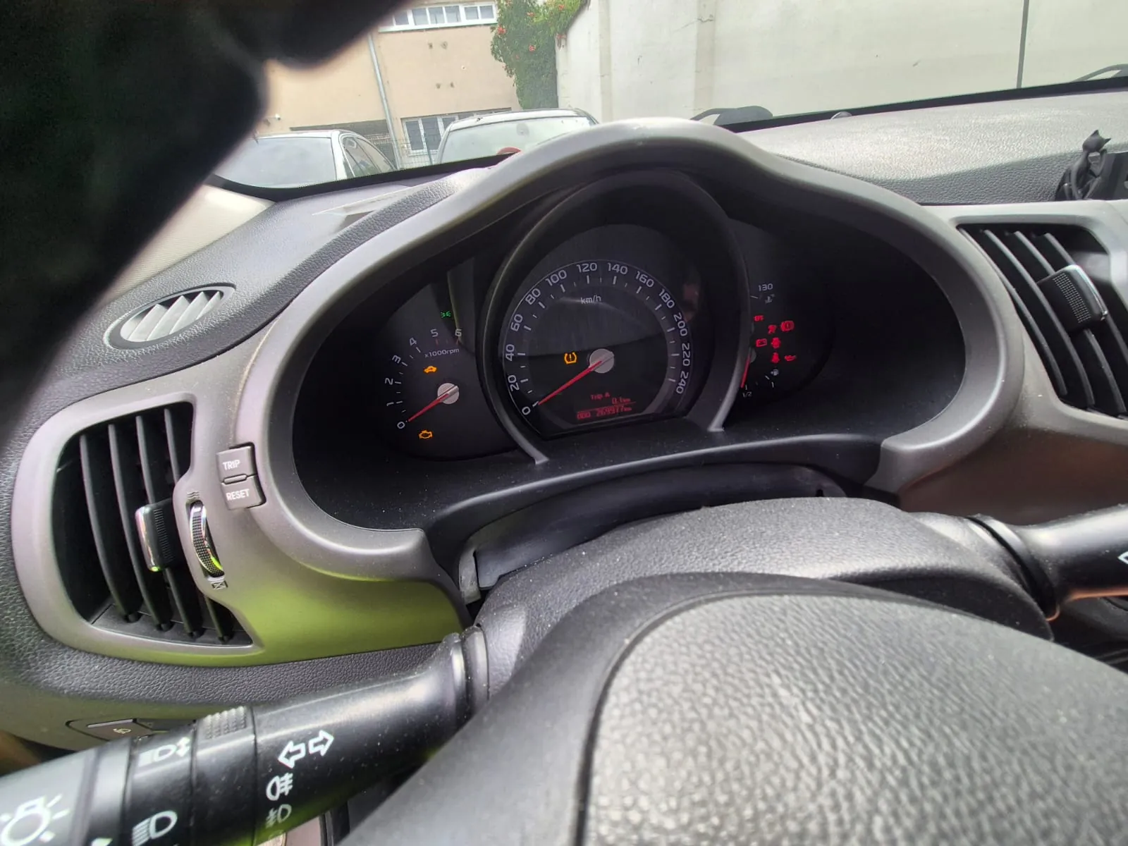 Widok z wnętrza samochodu na deskę rozdzielczą i zestaw wskaźników. W centrum znajduje się duży prędkościomierz z podziałką do 240 km/h, po lewej mniejszy obrotomierz, a po prawej wskaźnik paliwa i temperatury. Na wyświetlaczu cyfrowym widnieje data 26/09/2017. Widoczne są również kratki nawiewu, kierownica oraz dźwignia przełączników świateł z ikonami kierunkowskazów i świateł drogowych.