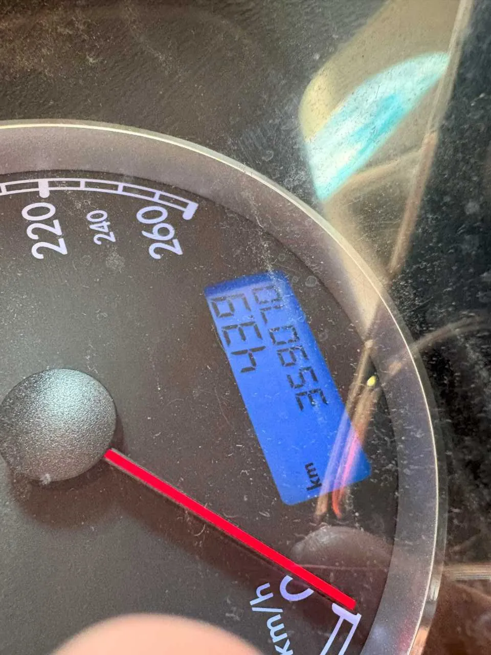 Zbliżenie na samochodowy wskaźnik prędkości. Czerwona igła wskazuje 0 km/h. Na niebieskim wyświetlaczu cyfrowym widoczne liczby 43.9 oraz 359070, obok oznaczenia 'km'. Skala prędkości sięga do 260 km/h z oznaczeniami 220, 240, 260.