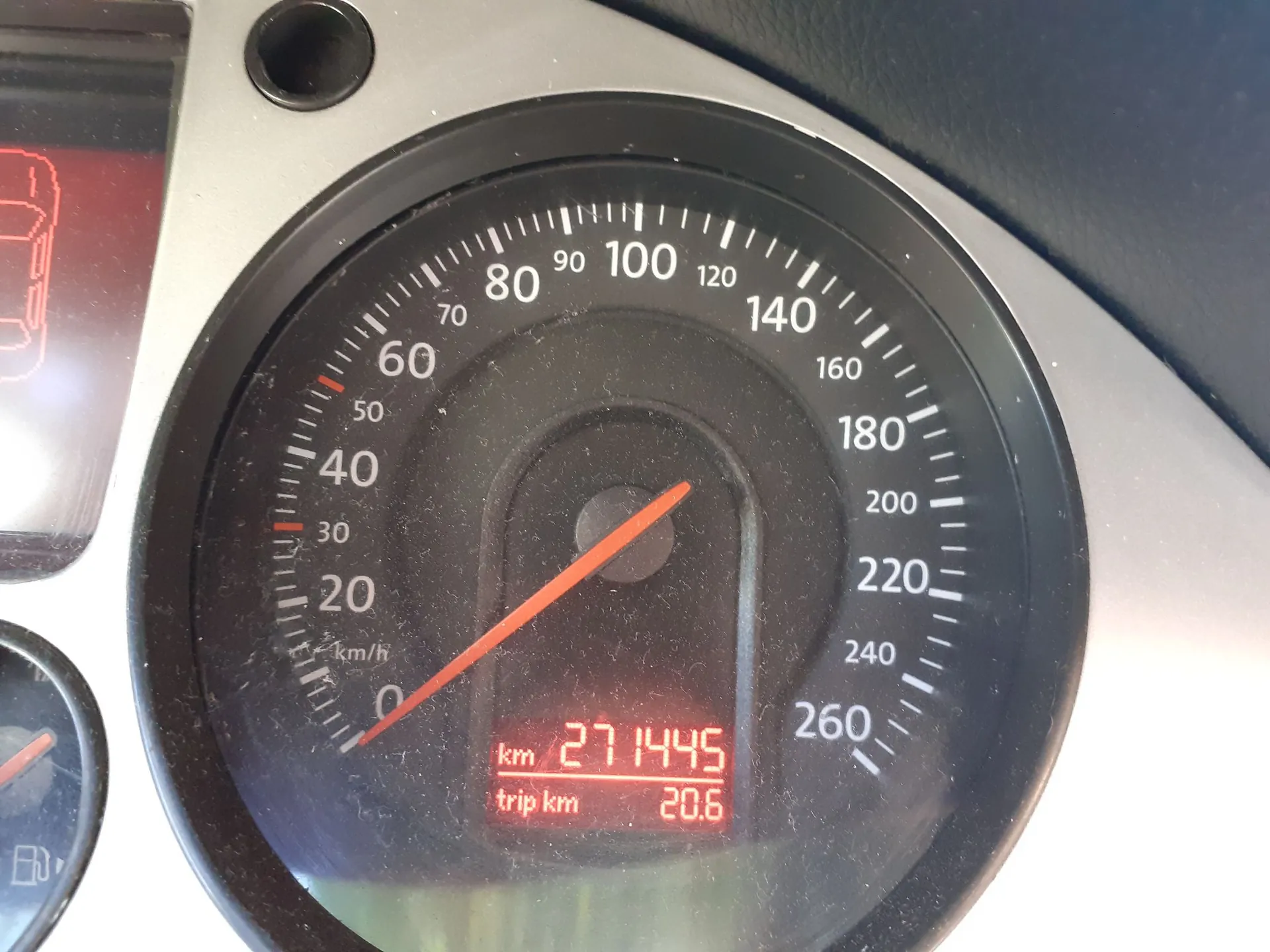 Zbliżenie na okrągły prędkościomierz w samochodzie. Skala prędkości sięga 260 km/h, a wskazówka wskazuje wartość 0. Na dole znajduje się cyfrowy wyświetlacz z pomarańczowym tekstem: 'km 271445' oraz 'trip km 20.6'.