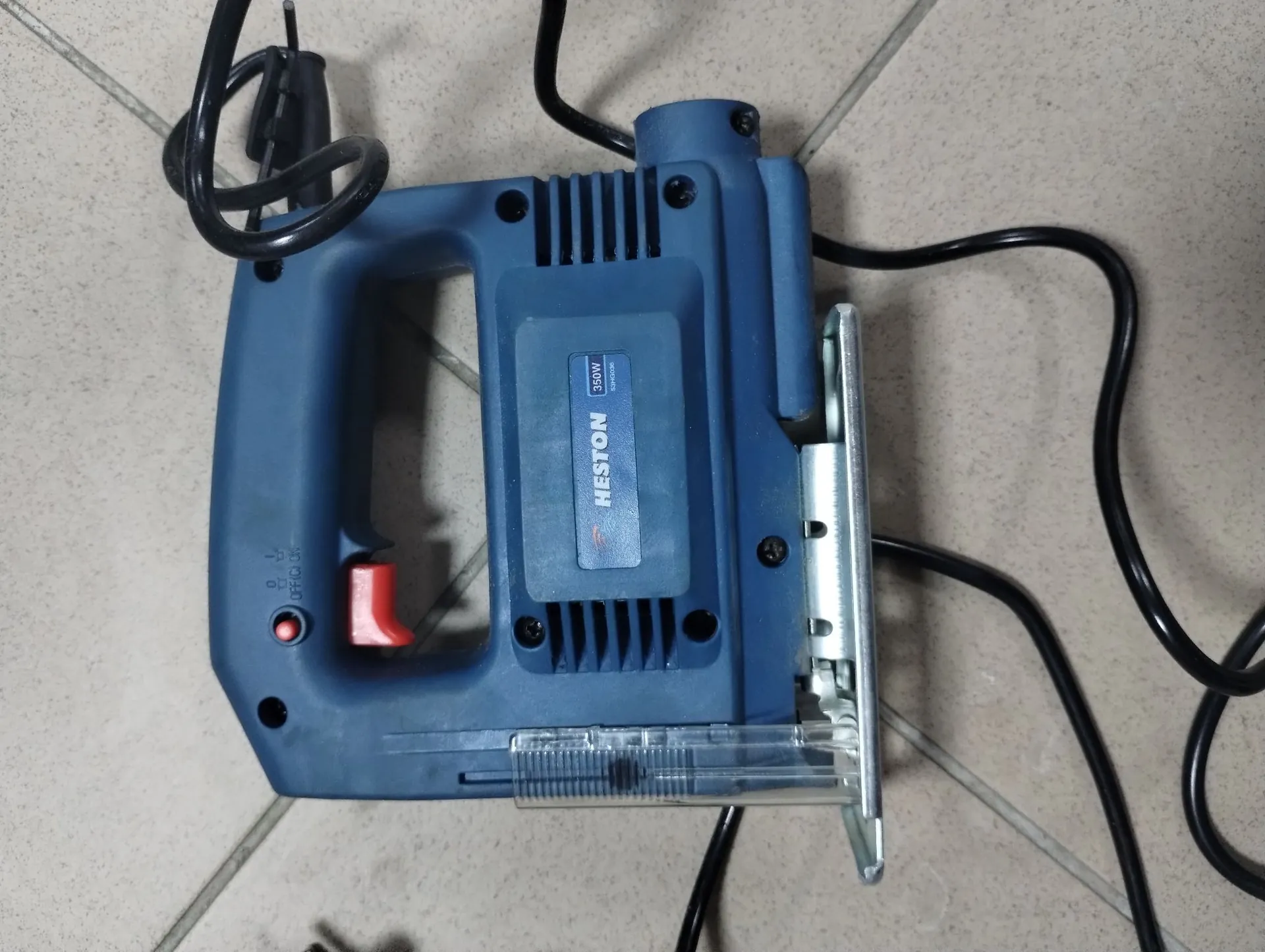 Niebieska wyrzynarka elektryczna marki HESTON o mocy 350W, leżąca na jasnej, kafelkowej powierzchni. Urządzenie posiada czarny kabel zasilający, czerwony przełącznik spustowy oraz przezroczystą osłonę stopy. Na obudowie znajduje się niebieska naklejka z białym napisem 'HESTON 350W'.