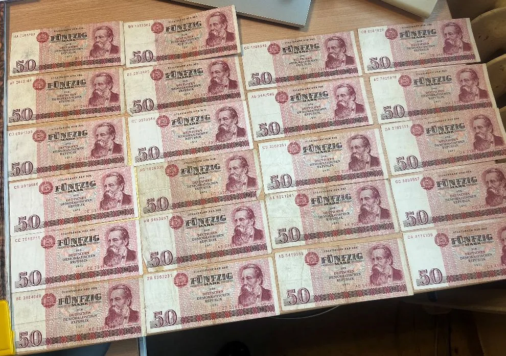 Kolekcja banknotów o nominale 50 marek z Niemieckiej Republiki Demokratycznej (NRD). Banknoty są ułożone w rzędach i kolumnach, na każdym widnieje napis 'FÜNFZIG MARK' oraz portret mężczyzny. Dominującym kolorem banknotów jest odcień czerwieni i brązu.