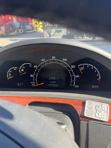 Widok z wnętrza pojazdu na deskę rozdzielczą. Centralnym elementem jest prędkościomierz z cyframi od 20 do 160 mph. Wewnątrz prędkościomierza znajduje się cyfrowy wyświetlacz pokazujący wartość 2488.1 MILES oraz numer 070901. Po lewej stronie widoczny jest wskaźnik poziomu paliwa oraz temperatury z wartością 62°F. Po prawej stronie znajduje się obrotomierz z oznaczeniem x1000 rpm. W prawym dolnym rogu widoczna jest godzina 8:44. Deska rozdzielcza ma wykończenie w kolorze ciemnego drewna, a w prawym dolnym rogu znajduje się srebrna, ozdobna tabliczka z reliefem.