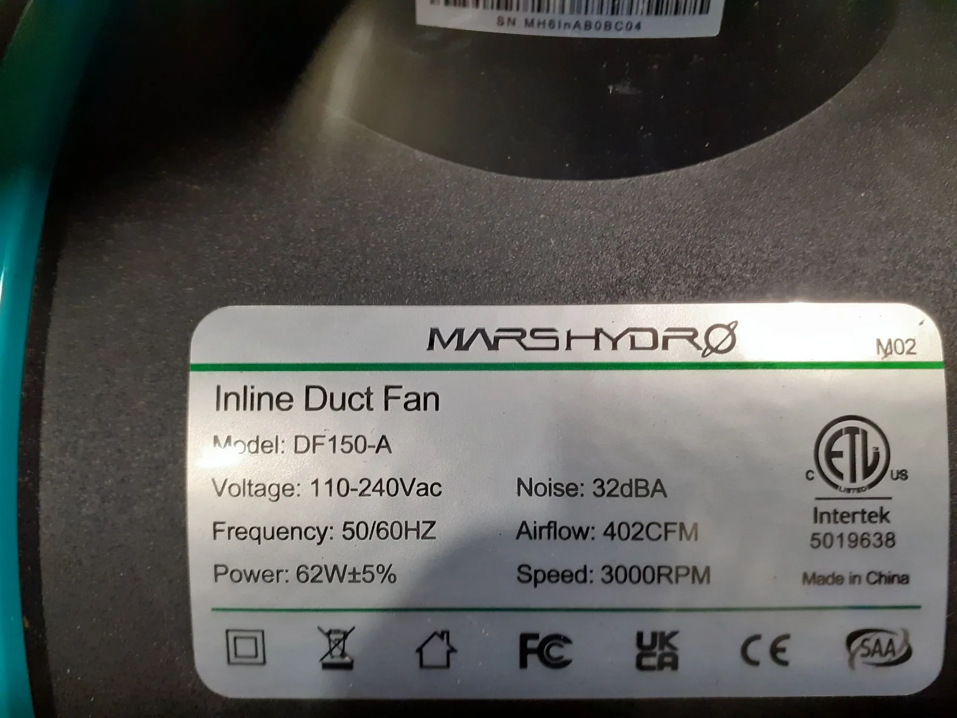 Zbliżenie na srebrną tabliczkę znamionową wentylatora kanałowego marki MARSHYDRO, model M02. Na tabliczce znajduje się tekst: 'Inline Duct Fan', 'Model: DF150-A', 'Voltage: 110-240Vac', 'Frequency: 50/60HZ', 'Power: 62W±5%', 'Noise: 32dBA', 'Airflow: 402CFM', 'Speed: 3000RPM' oraz informacja 'Made in China'. Widoczne są również certyfikaty i symbole: logo ETL Intertek (numer 5019638), symbol podwójnej izolacji, przekreślony kosz na śmieci, symbol domu, FC, UKCA, CE oraz SAA.