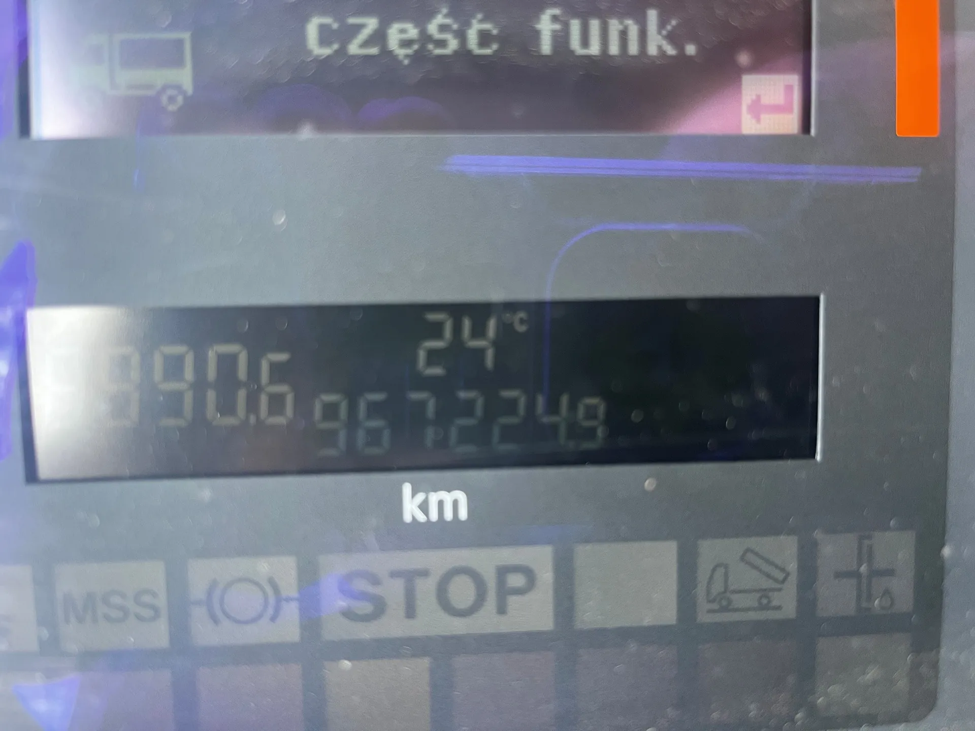 Zbliżenie na cyfrowy wyświetlacz w pojeździe. Na górnym ekranie widnieje napis 'część funk.' oraz ikona ciężarówki. Na dolnym, ciemniejszym wyświetlaczu widoczne są liczby: '890.6', '24°C' oraz '967224.9' z jednostką 'km' poniżej. Pod ekranem znajdują się napisy 'MSS', symbol hamulca ręcznego w nawiasie oraz napis 'STOP', a obok nich dwie ikony techniczne.