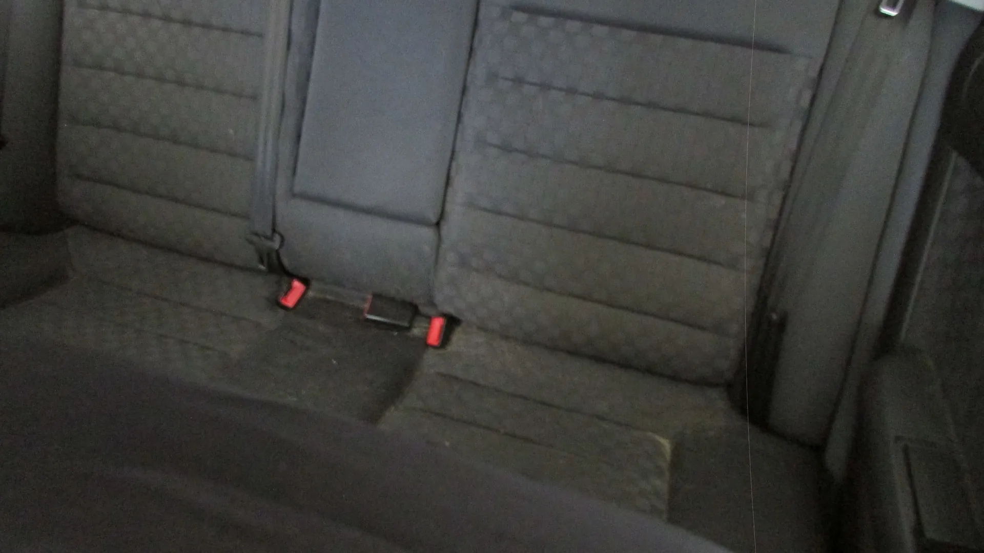 Zdjęcie przedstawiające tylną kanapę w samochodzie. Siedziska i oparcia są obite ciemnoszarym materiałem o prążkowanej strukturze. Widoczne są dwa czerwone przyciski zapięć pasów bezpieczeństwa.