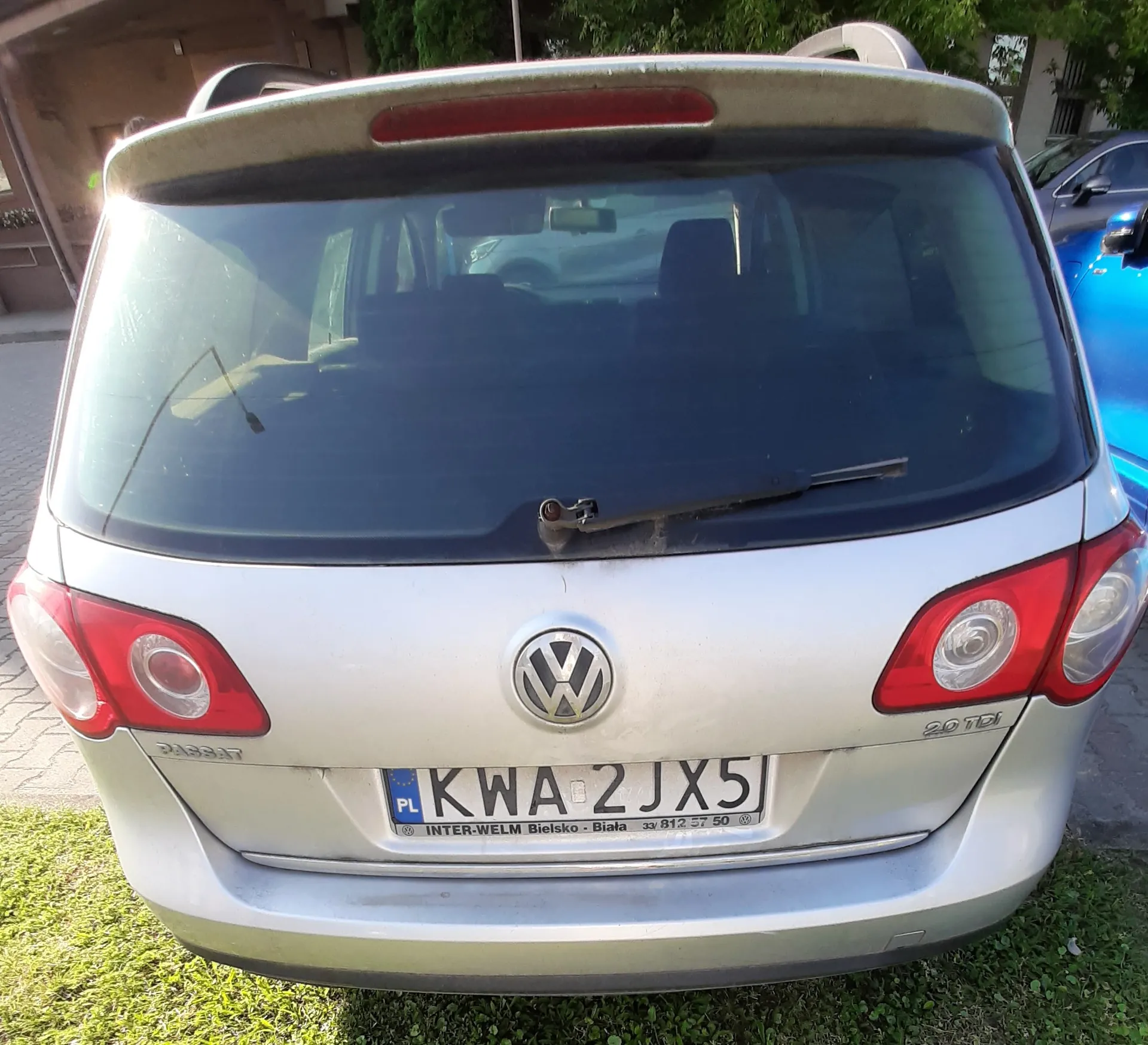 Tylny widok srebrnego samochodu marki Volkswagen Passat. Na klapie bagażnika znajduje się logo Volkswagena, napis 'PASSAT' po lewej stronie oraz '2.0 TDI' po prawej. Samochód ma polską tablicę rejestracyjną o numerze KWA 2JX5. Poniżej tablicy widnieje napis 'INTER-WELM Bielsko-Biała 33 812 57 50'.