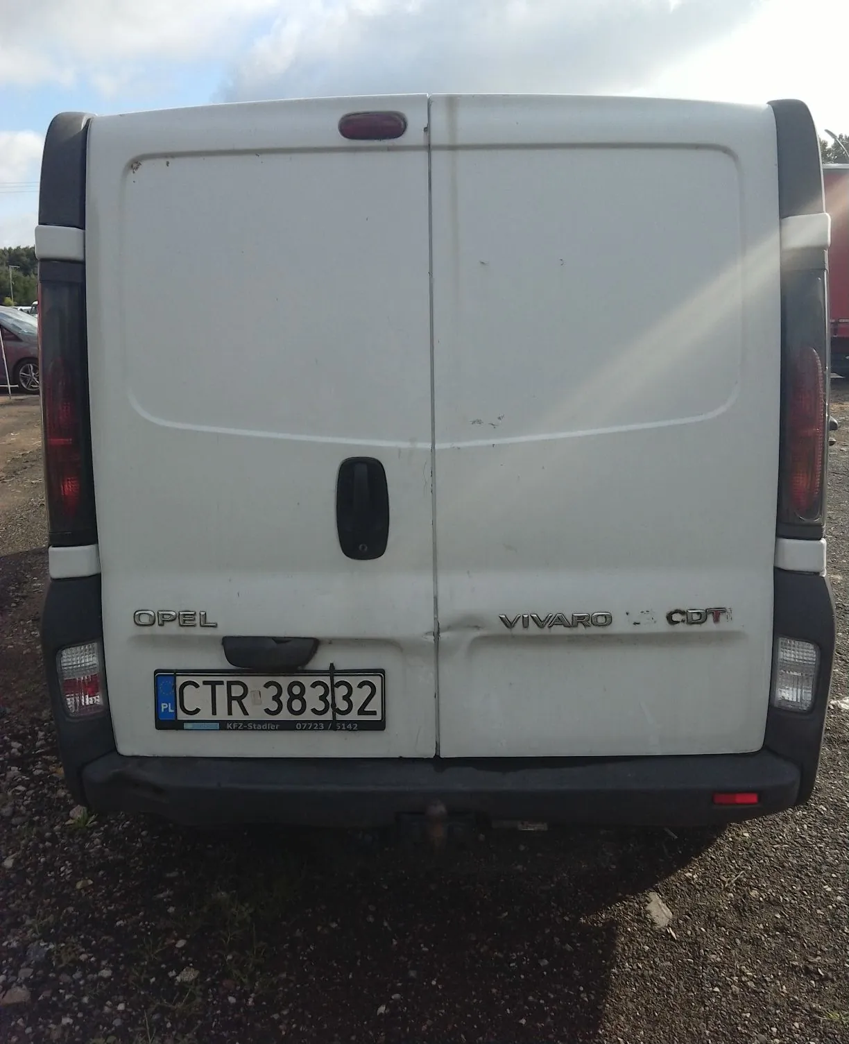 Tylny widok białego samochodu dostawczego marki Opel Vivaro CDT. Pojazd posiada dwie tylne klapy, czarne plastikowe zderzaki oraz tablicę rejestracyjną o numerze CTR 38332 z oznaczeniem PL. Na zderzaku widnieje napis KFZ-Stadler oraz numer telefonu 07723 / 7142.