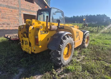 Żółty ładowacz teleskopowy marki JCB, model 530, zaparkowany na trawiastym terenie obok budynku w budowie z czerwonej cegły. Maszyna jest widoczna z boku i z tyłu, posiada duże, terenowe opony i przeszkloną kabinę operatora.