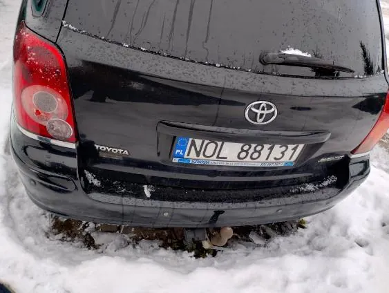 Tył czarnego samochodu marki Toyota zaparkowanego na śniegu. Widoczna tablica rejestracyjna z napisem NOL 88131 oraz oznaczeniem PL po lewej stronie. Na bagażniku umieszczono logo Toyoty i napis TOYOTA po lewej stronie. Samochód pokryty jest śniegiem, szczególnie na szybie tylnej i zderzaku. W tle widoczny śnieg na ziemi.