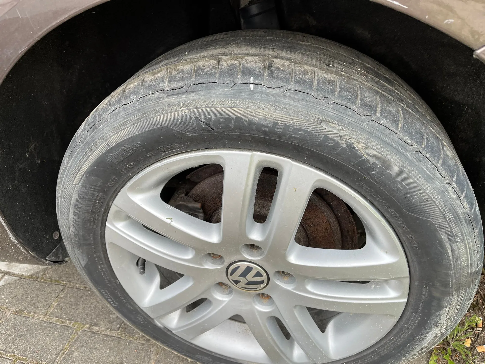 Zbliżenie na koło samochodu z oponą marki Hankook Ventus Prime. Opona wykazuje oznaki zużycia i pęknięcia na bieżniku. Srebrna felga aluminiowa z logo Volkswagena w centrum.