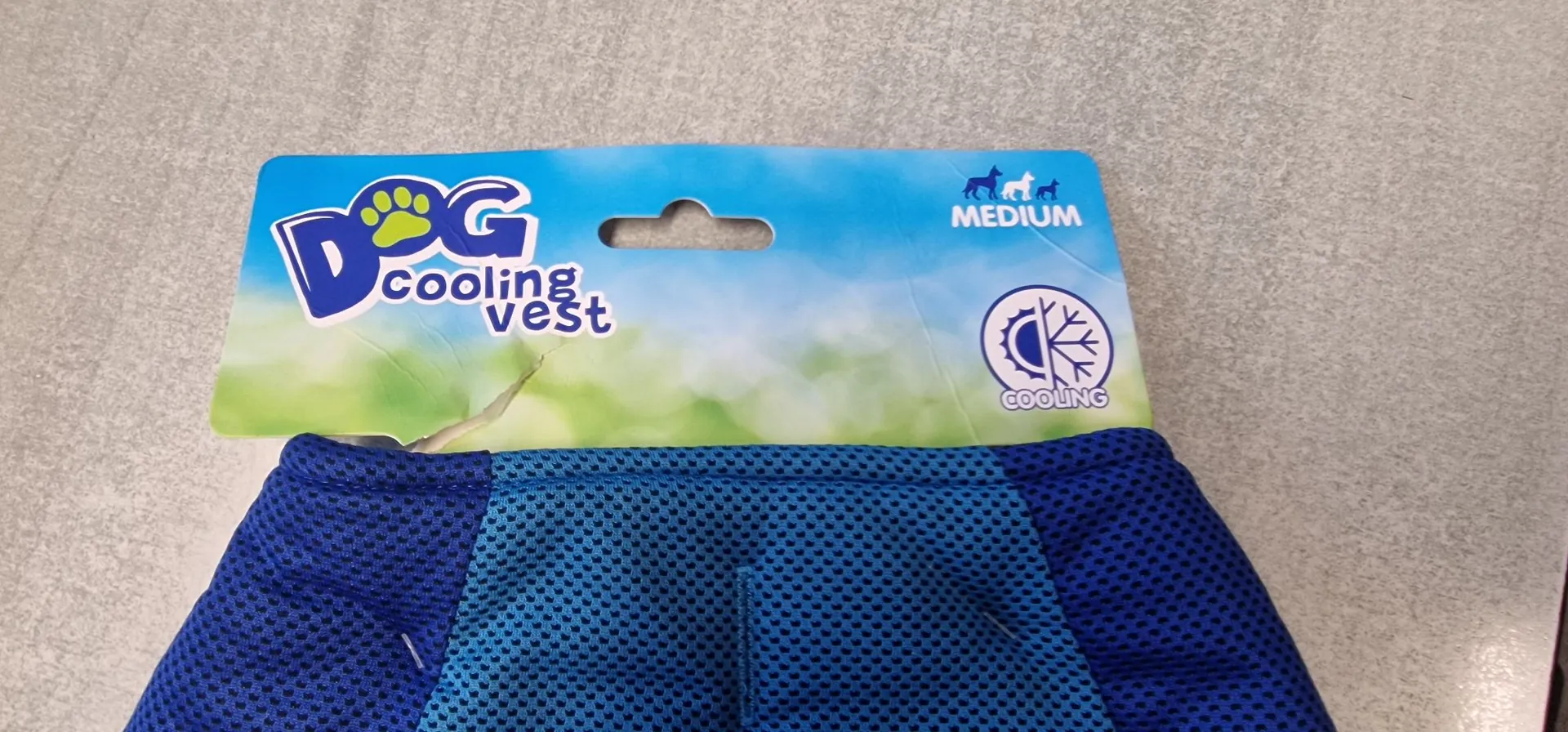 Niebieska chłodząca kamizelka dla psa z dołączoną tekturową etykietą. Na etykiecie znajduje się napis 'Dog COOLING Vest', informacja o rozmiarze 'MEDIUM' oraz grafika przedstawiająca słońce i płatek śniegu z napisem 'COOLING'.