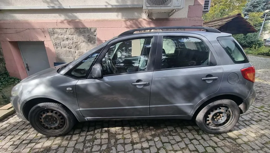 Szary samochód typu hatchback zaparkowany bokiem na kostce brukowej przed jasnym budynkiem. Pojazd posiada czarne relingi dachowe i stalowe felgi bez kołpaków.