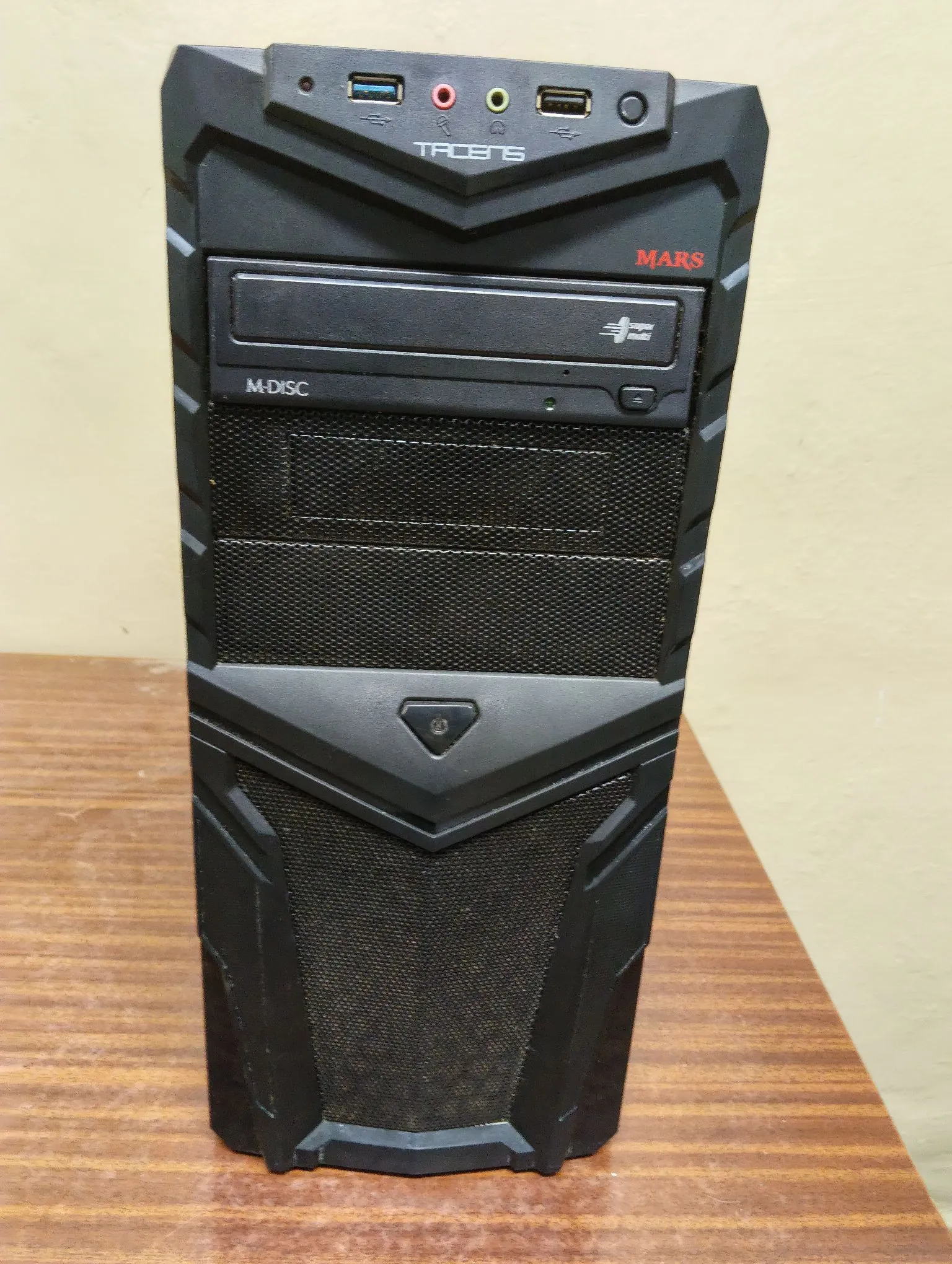 Czarna obudowa komputera stacjonarnego typu tower z napędem optycznym. Na górnym panelu znajdują się porty USB, gniazda audio oraz przycisk zasilania z napisem 'TALENS'. Na przednim panelu widnieje czerwony napis 'MARS' oraz oznaczenie 'M-DISC' przy napędzie DVD. Obudowa ma agresywny, kanciasty design z elementami w formie siatki wentylacyjnej.