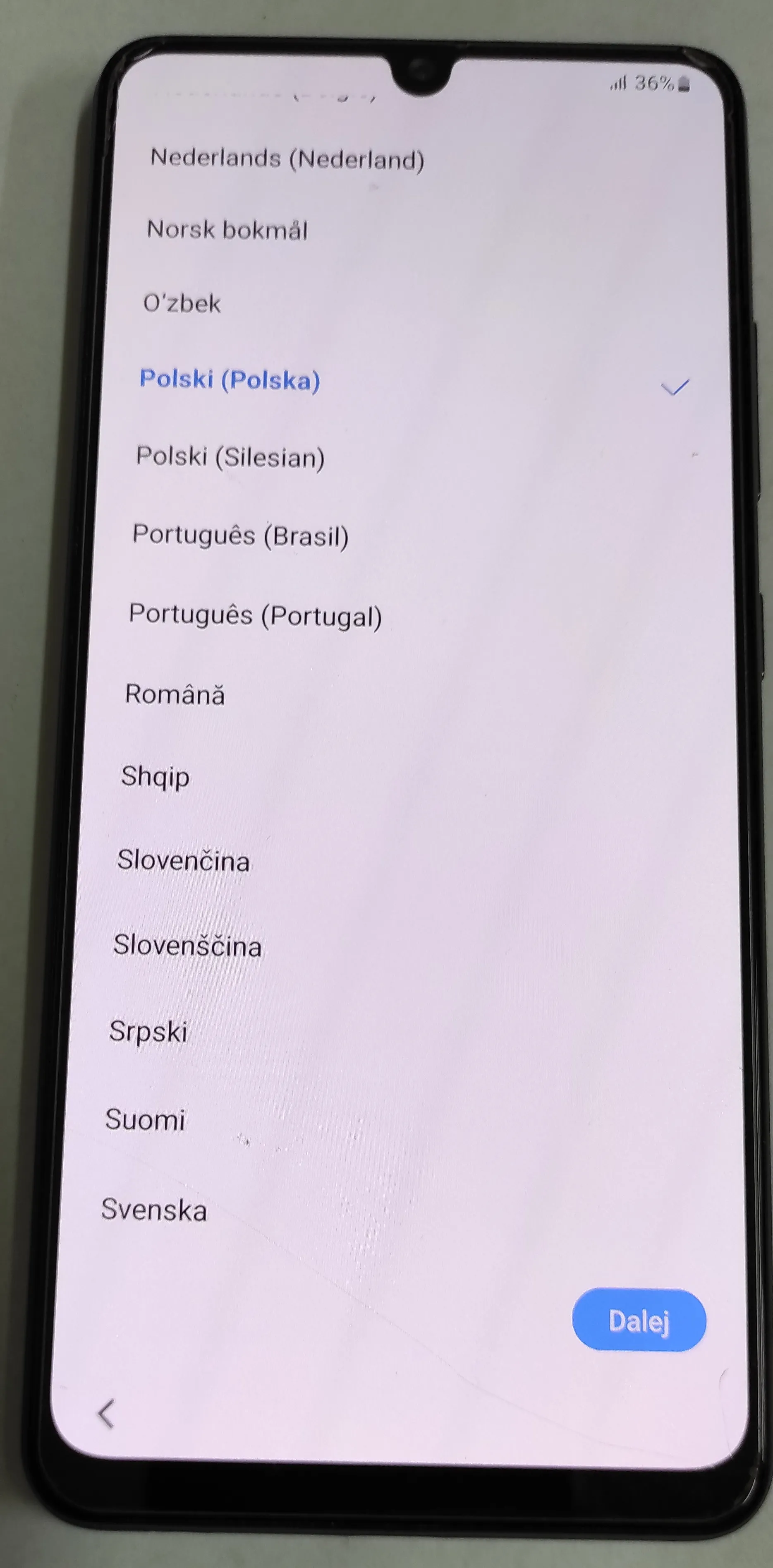 Zdjęcie ekranu smartfona wyświetlającego listę wyboru języka. Na liście widoczne są m.in. języki: Nederlands (Nederland), Norsk bokmål, O'zbek, Polski (Polska) - zaznaczony na niebiesko, Polski (Silesian), Português (Brasil), Português (Portugal), Română, Shqip, Slovenčina, Slovenščina, Srpski, Suomi oraz Svenska. W prawym dolnym rogu znajduje się niebieski przycisk z napisem 'Dalej'.