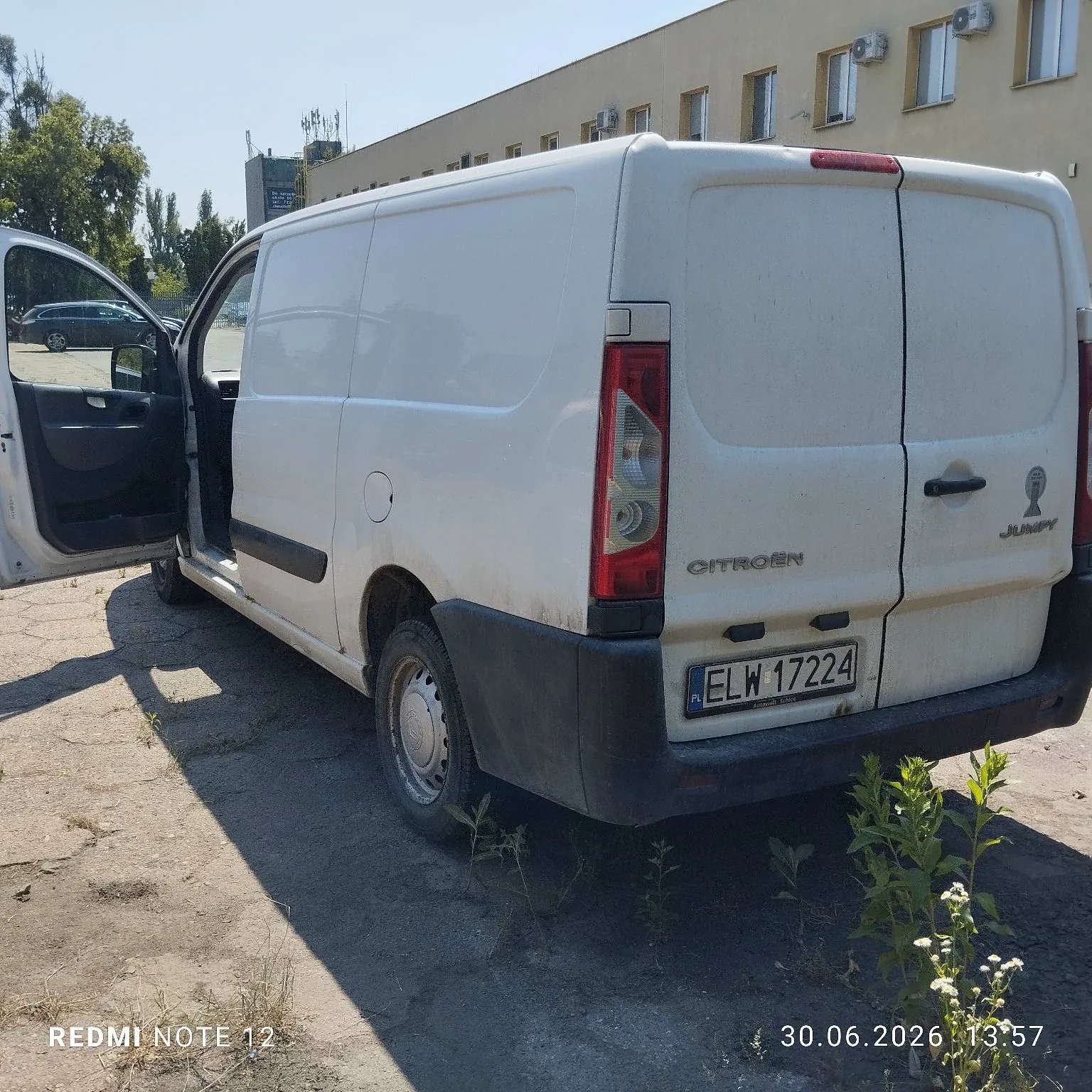 Biały samochód dostawczy marki Citroen Jumpy zaparkowany na betonowym podłożu. Widoczny jest tył i prawy bok pojazdu z otwartymi przednimi drzwiami po stronie kierowcy. Samochód ma polską tablicę rejestracyjną o numerze ELW 17224. W tle znajduje się jasny budynek oraz drzewa. Na dole zdjęcia widnieje napis 'REDMI NOTE 12' oraz data i godzina '30.06.2026 13:57'.