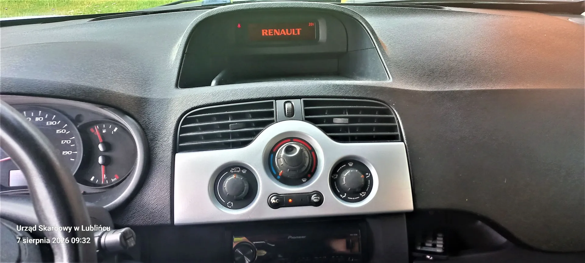 Wnętrze samochodu marki Renault, widok na deskę rozdzielczą. W górnej części znajduje się czerwony wyświetlacz z napisem 'RENAULT'. Poniżej znajdują się poziome kratki nawiewu oraz srebrny panel z trzema pokrętłami do regulacji klimatyzacji i temperatury. Po lewej stronie widoczny jest fragment licznika prędkości oraz kierownicy. Na dole znajduje się radio marki Pioneer. W lewym dolnym rogu zdjęcia widnieje biały napis: 'Urząd Skarbowy w Lublińcu 7 sierpnia 2026 09:32'.