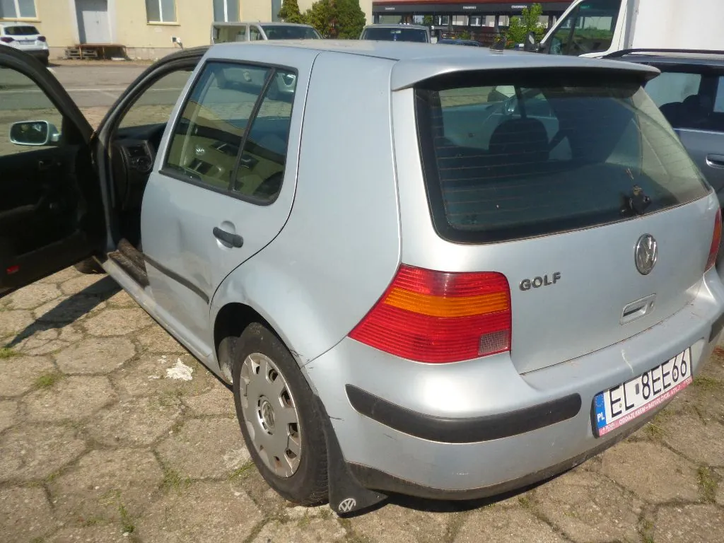Srebrny samochód marki Volkswagen Golf zaparkowany na betonowym podjeździe. Widok z tyłu i z boku, lewe tylne drzwi są otwarte. Na tylnej klapie znajduje się napis GOLF oraz logo Volkswagena. Samochód ma polską tablicę rejestracyjną o numerze EL 8EE66. Na tylnym lewym błotniku widoczne jest wgniecenie.