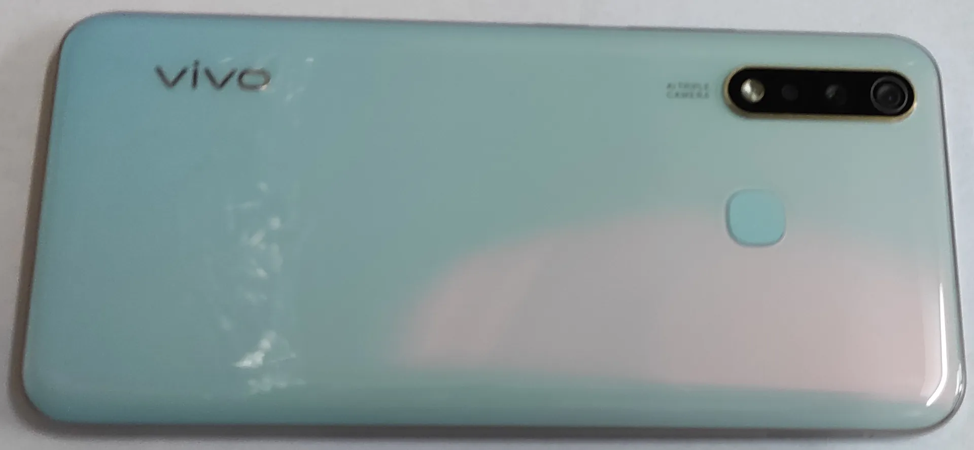 Jasnoniebieski smartfon marki vivo pokazany od tyłu. W lewym górnym rogu znajduje się napis 'vivo', a w prawym górnym rogu poziomy moduł z trzema obiektywami aparatu i napisem 'AI TRIPLE CAMERA'. Na środku obudowy widoczny jest okrągły czytnik linii papilarnych.