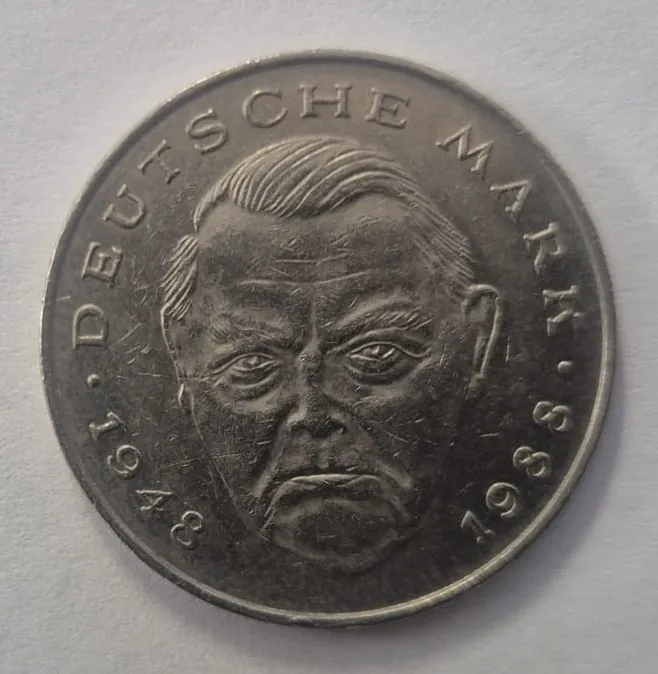 Srebrzysta moneta z wizerunkiem mężczyzny w profilu trzech czwartych. Wzdłuż górnej krawędzi widnieje napis „DEUTSCHE MARK”, a po bokach daty „1948” po lewej i „1988” po prawej stronie.