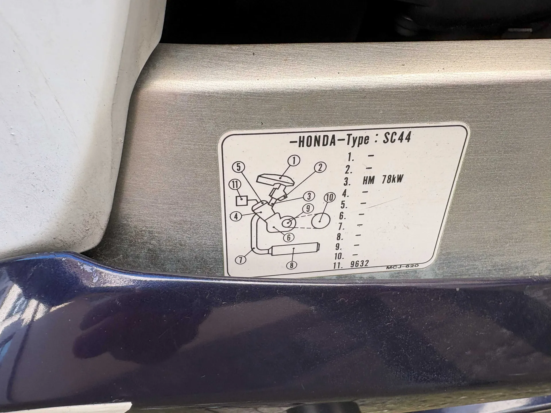 Biała etykieta z czarnym tekstem i schematem zamontowana na metalowej powierzchni. Na etykiecie widnieje napis "-HONDA-Type: SC44" oraz schemat z oznaczeniami od 1 do 11. Po prawej stronie schematu lista numerowana od 1 do 11 z wartościami: 1. -, 2. -, 3. HM 78kW, 4. -, 5. -, 6. -, 7. -, 8. -, 9. -, 10. -, 11. 9632. W prawym dolnym rogu etykiety napis "MCJ-620". W tle metalowa powierzchnia i fragment białego obiektu po lewej stronie.