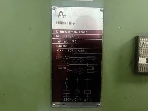 Metalowa tabliczka znamionowa zamontowana na zielonej powierzchni. Na górze znajduje się logo Thyssen oraz napis 'Hüller Hille'. Poniżej widnieją dane: 'D-5810 Witten-Annen', 'Nr. 6160469.0', 'Typ nbh 70', 'Baujahr 1983' oraz numer seryjny 'Nr 6280380012'. W dolnej części tabliczki znajduje się schemat elektryczny z oznaczeniami: '36 kVA', '3~ 380 V', '50 Hz', '56 A' oraz napięcia wyjściowe '~220V', '24 V', '24 V'.