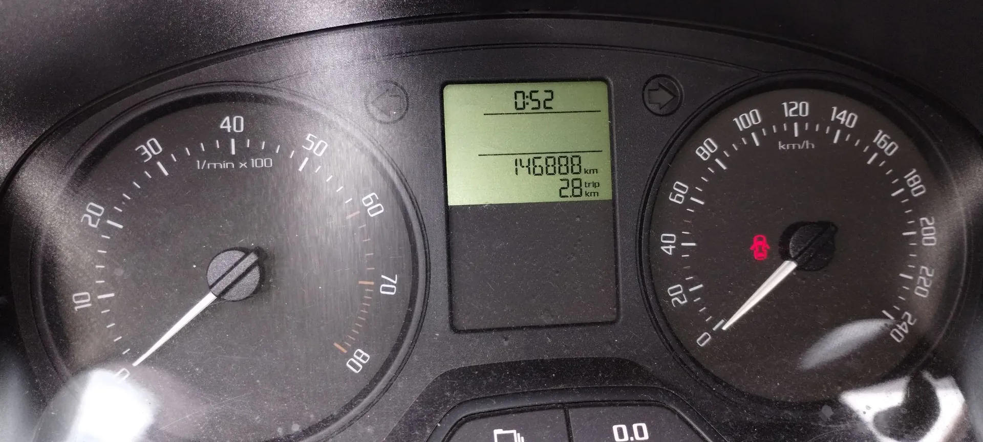 Zbliżenie na deskę rozdzielczą pojazdu. Po lewej stronie znajduje się obrotomierz z podziałką od 10 do 80 (1/min x 100). Po prawej stronie prędkościomierz z podziałką od 0 do 240 km/h. W centralnej części znajduje się cyfrowy wyświetlacz LCD, na którym widnieje godzina 0:52, przebieg 146888 km oraz licznik trip 2.8 km.