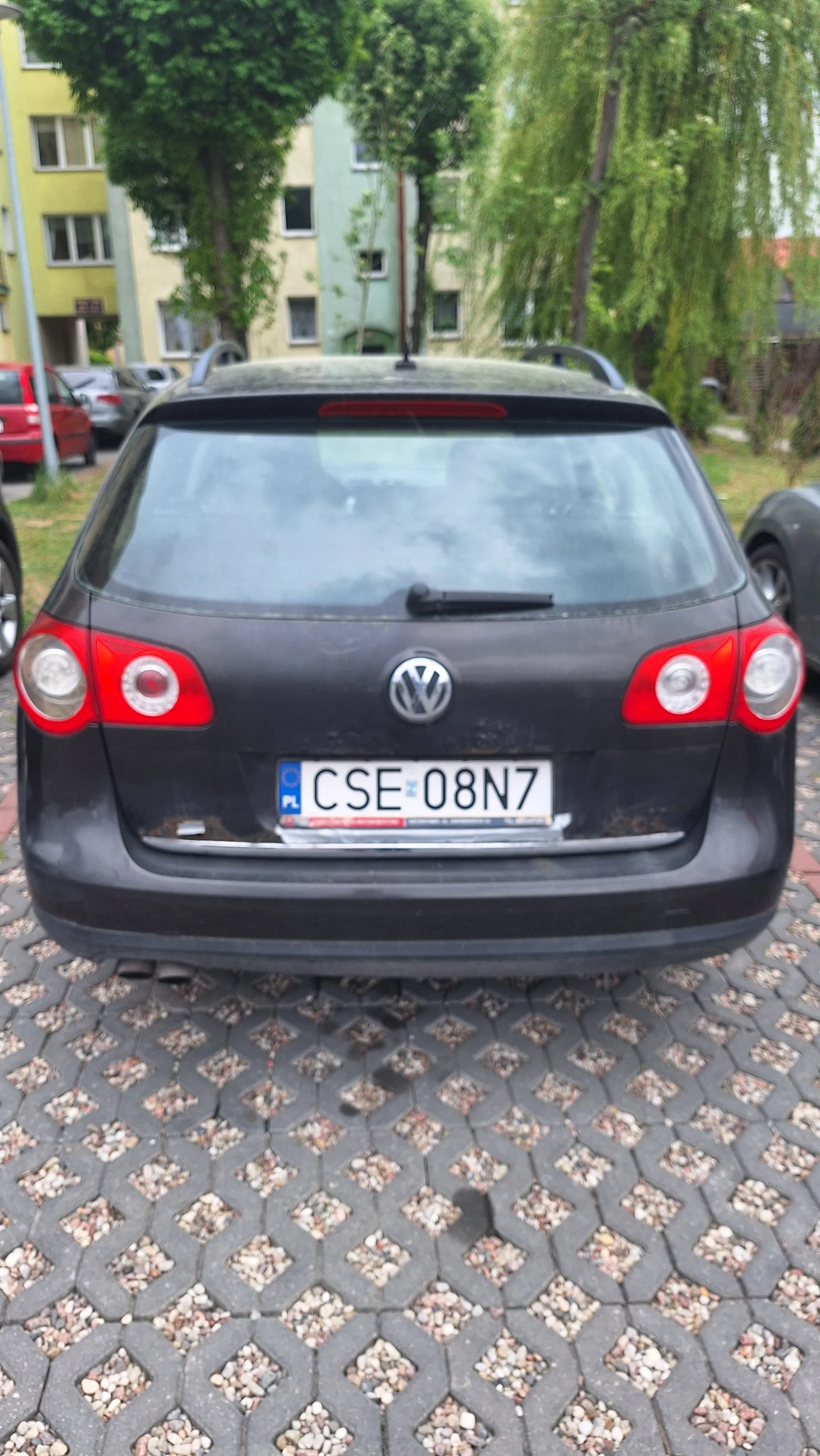 Czarny samochód marki Volkswagen z tablicą rejestracyjną CSE 08N7, zaparkowany na brukowanej powierzchni. W tle widoczne są budynki mieszkalne, drzewa oraz inne pojazdy. Tablica rejestracyjna umieszczona jest pionowo, co wskazuje na nieprawidłową orientację obrazu.