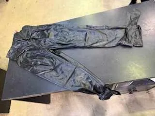 Czarna para spodni leżąca na ciemnym stole. Spodnie są pomarszczone, a stół znajduje się na jasnej podłodze.