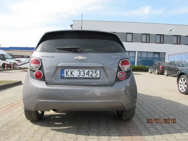 Tył szarego samochodu Chevrolet z tablicą rejestracyjną KK 33425. W tle budynek z oknami, inne zaparkowane pojazdy oraz data 30/01/2010 w prawym dolnym rogu. Samochód stoi na brukowanej powierzchni.