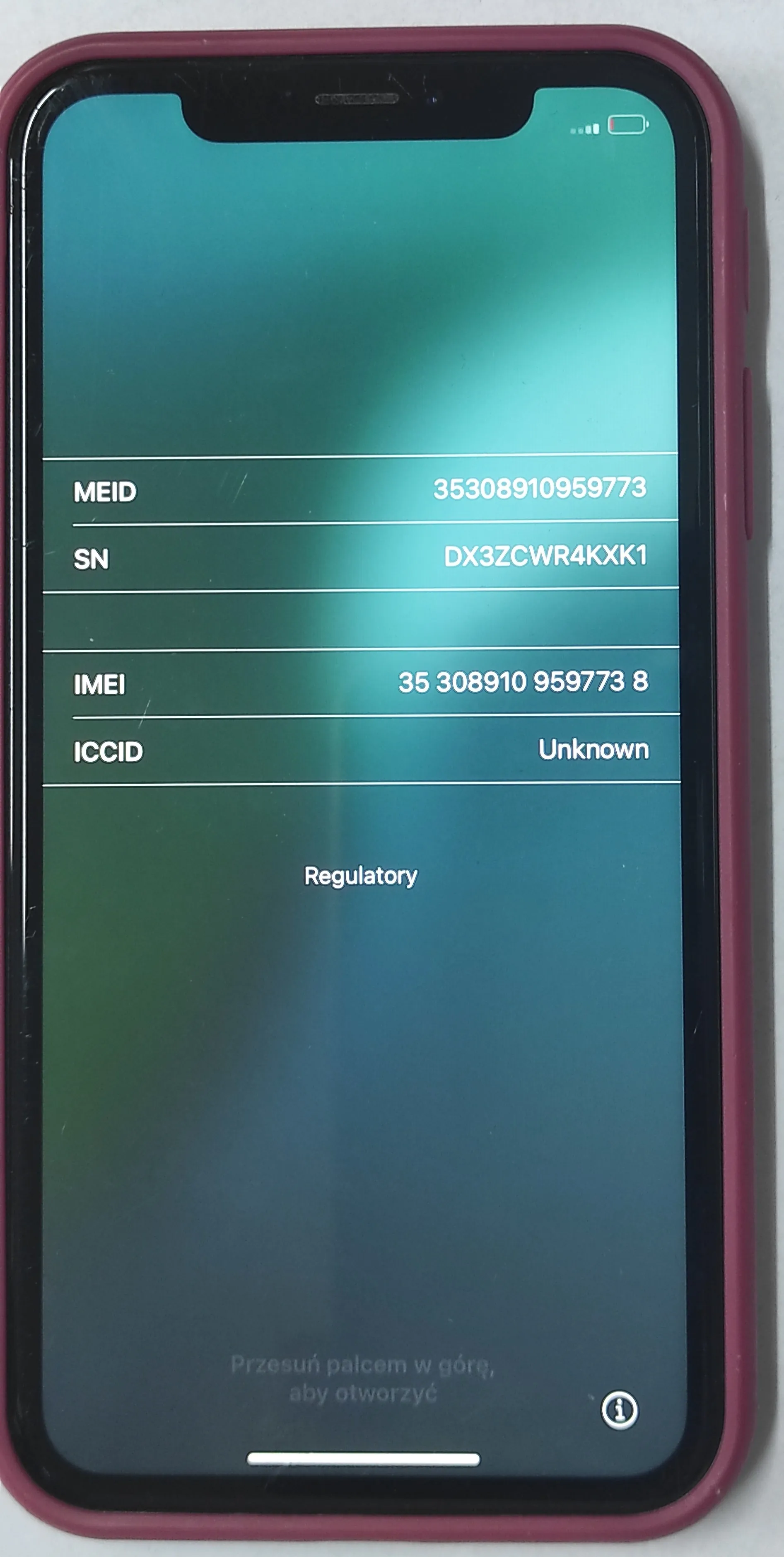 Ekran smartfona w bordowej obudowie wyświetlający informacje o urządzeniu na niebiesko-zielonym tle. Widoczne są następujące dane: MEID: 35308910959773, SN: DX3ZCWR4KXK1, IMEI: 35 308910 959773 8, ICCID: Unknown. Poniżej znajduje się napis 'Regulatory'. Na dole ekranu widnieje tekst: 'Przesuń palcem w górę, aby otworzyć' oraz ikona informacji w kółku.